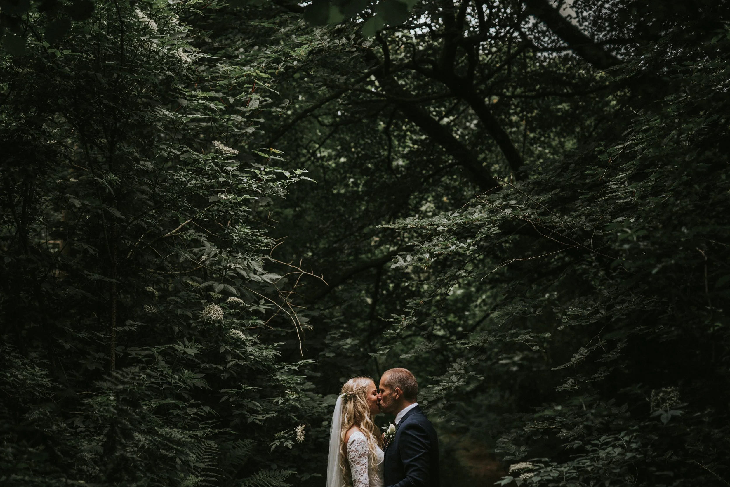 A bride and groom sharing a kiss in a lush, green forest.