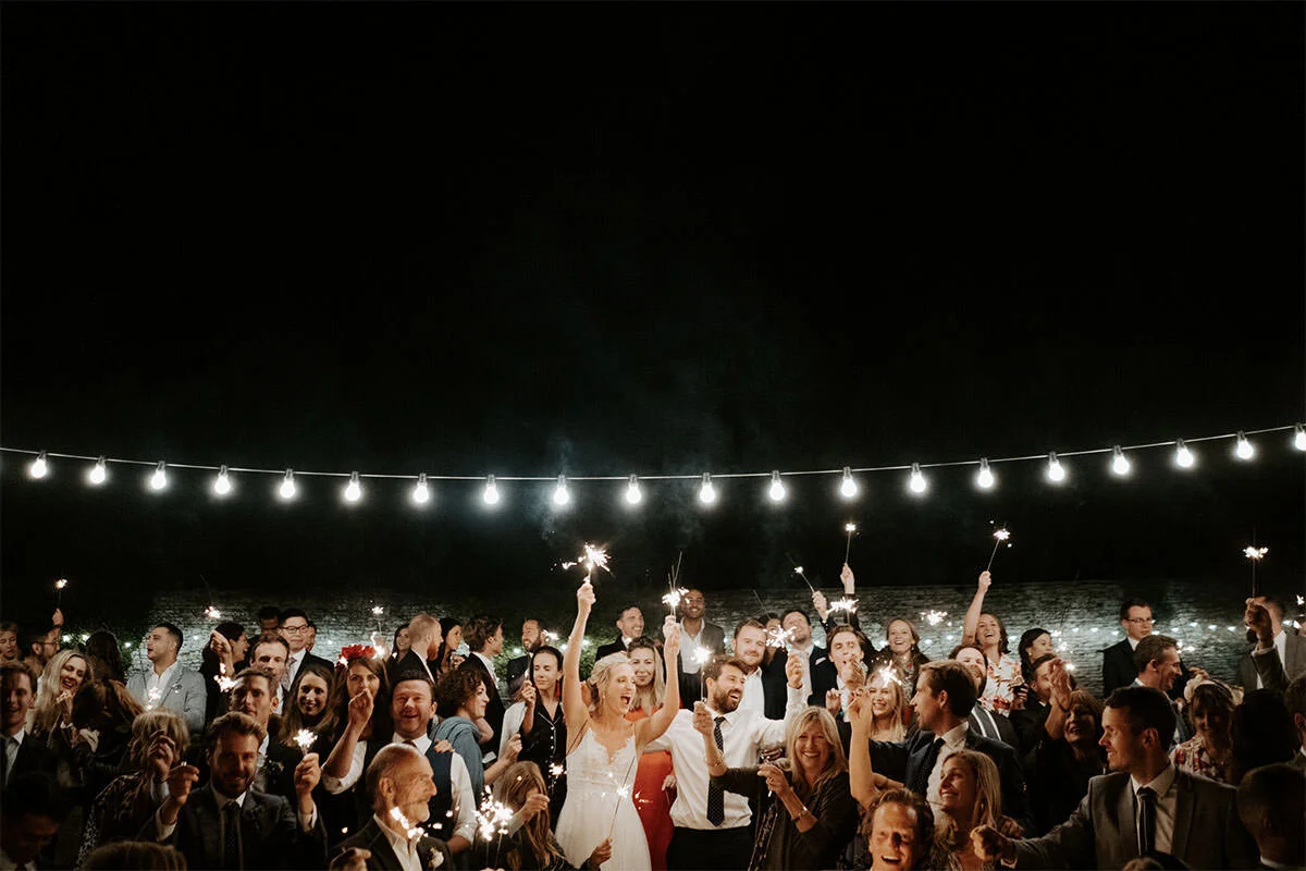 Crowd celebrating at night with sparklers and string lights overhead