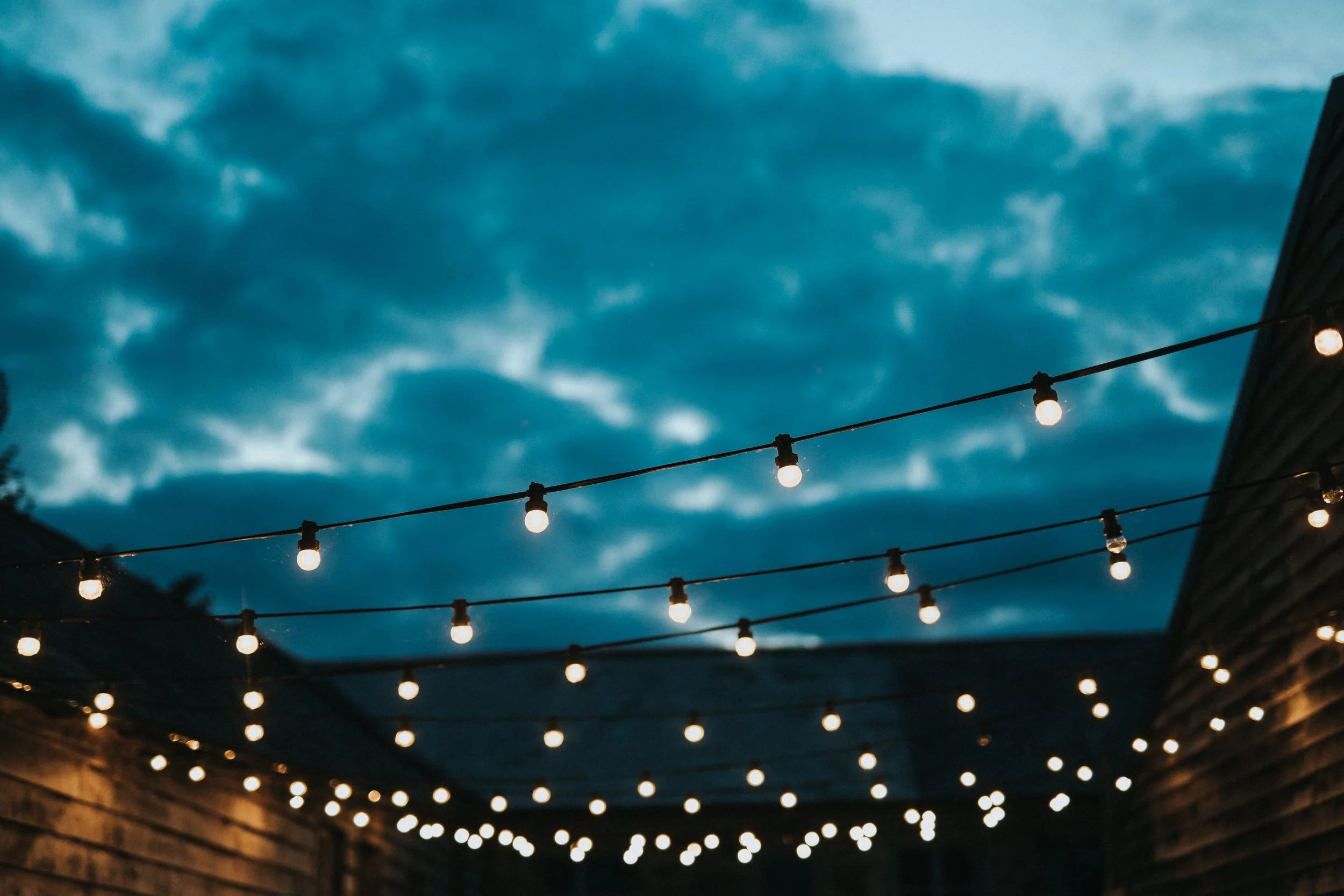 String of outdoor string lights illuminated against a cloudy evening sky.