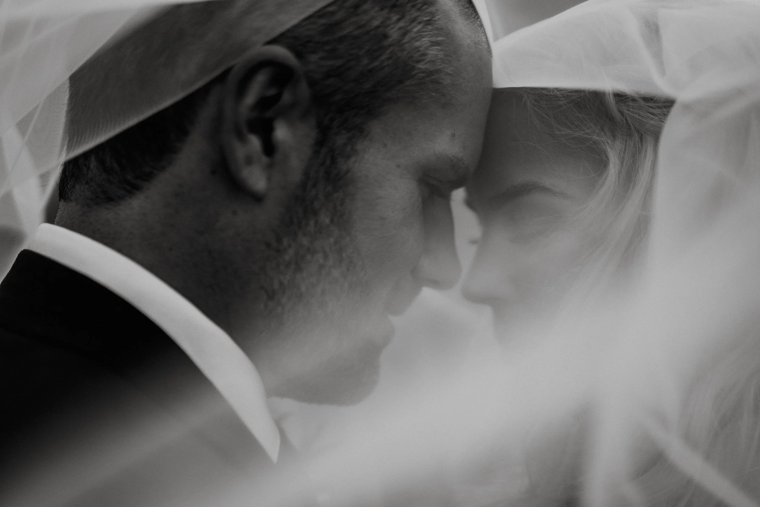 A black and white close-up of a bride and groom with their foreheads touching, eyes closed, sharing an intimate moment.