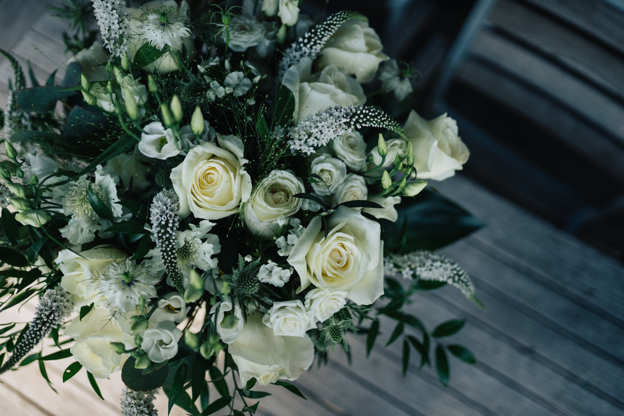 A bouquet of white flowers, including roses and other blossoms, placed on a wooden surface.