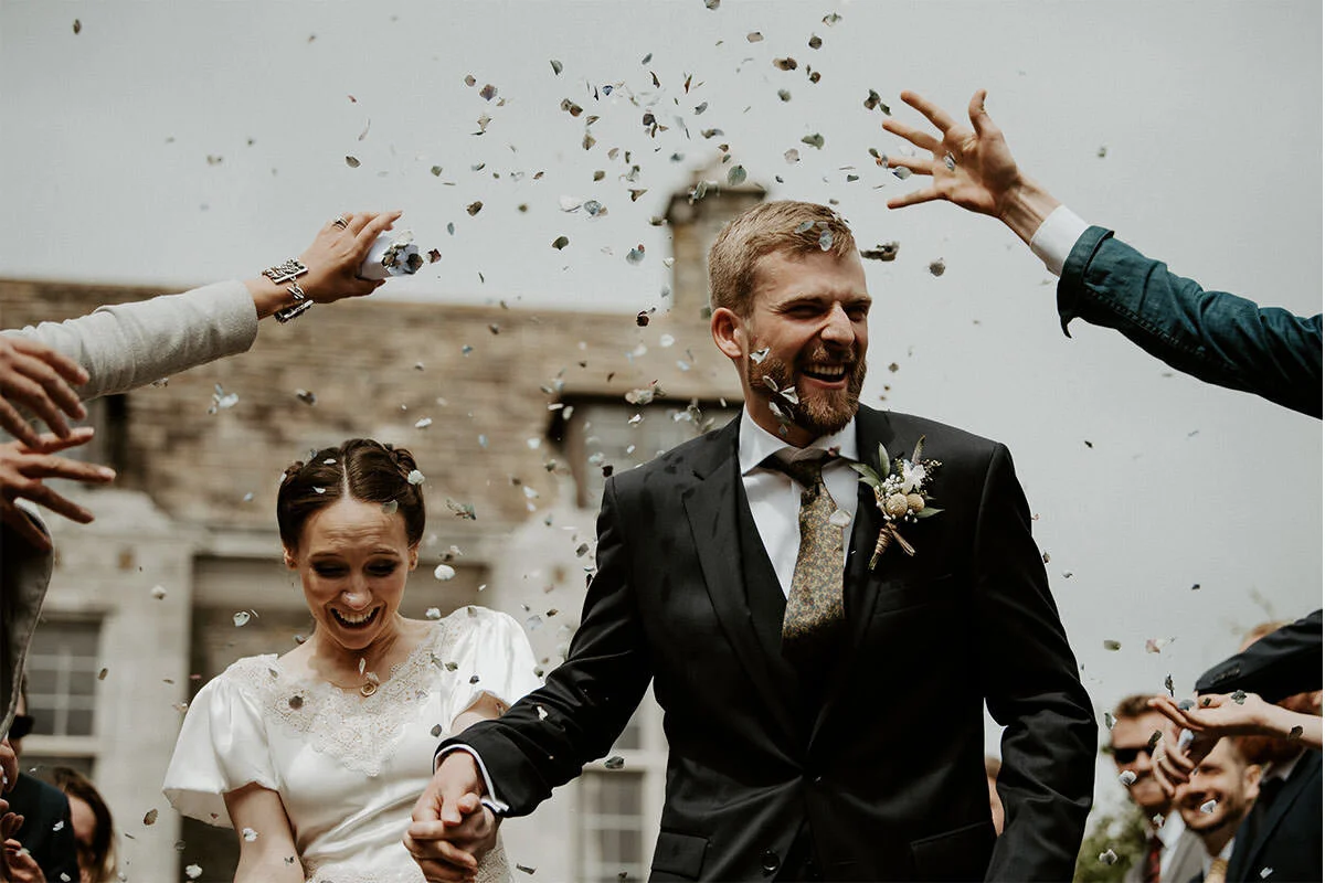 A couple in wedding attire celebrating surrounded by confetti outdoors.