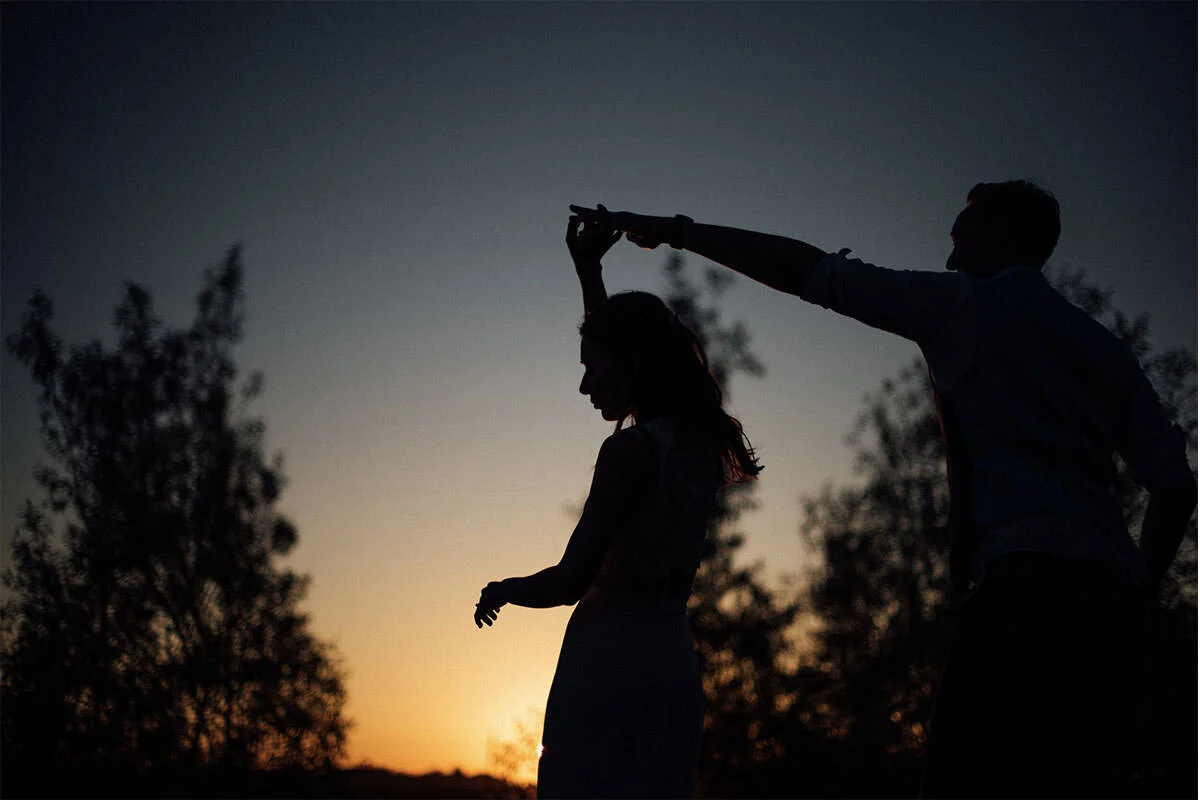 Silhouette of a man twirling a woman during sunset with trees in the background.
