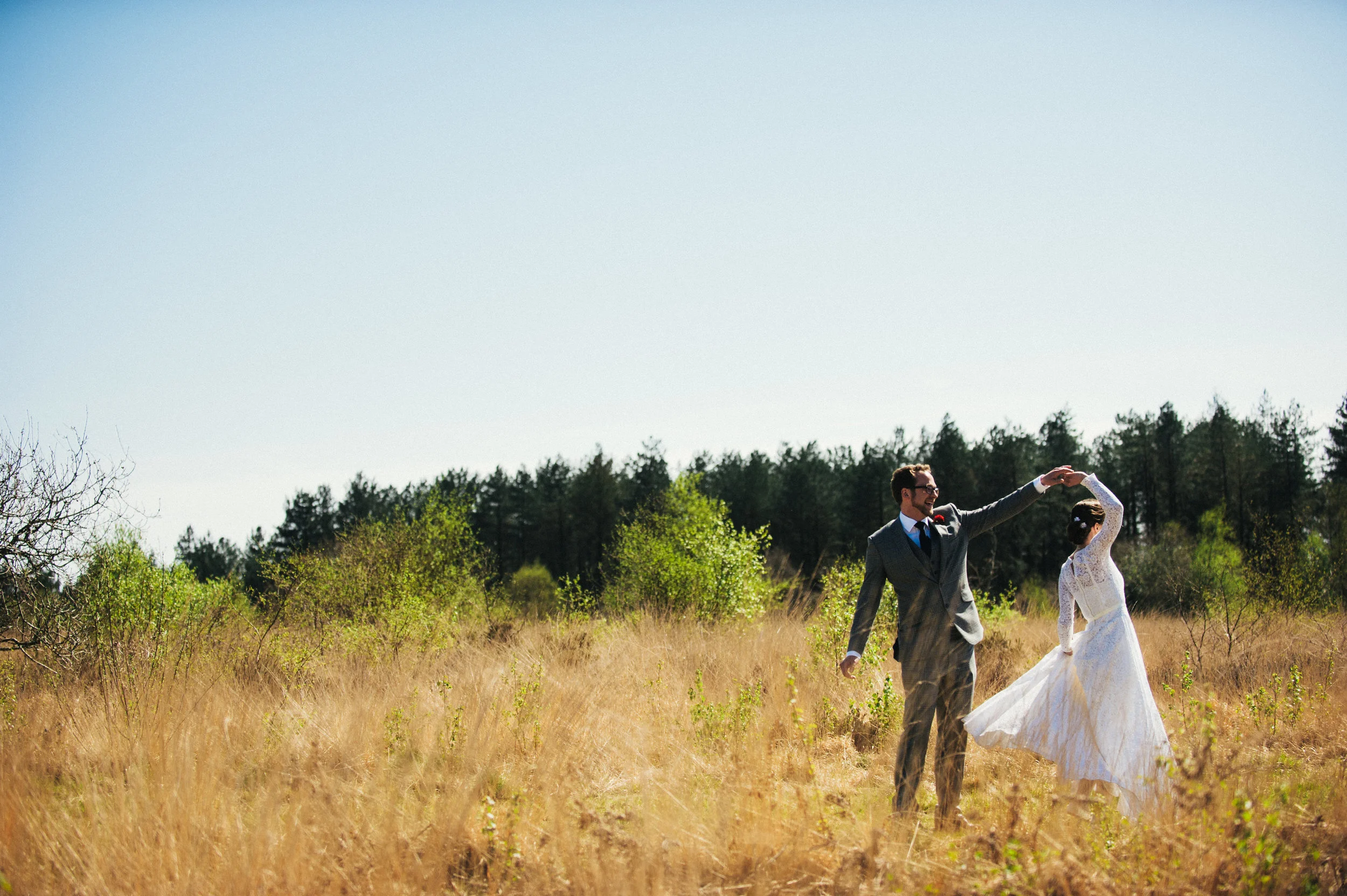 A man and woman dancing in a grassy field with trees in the background on a sunny day.