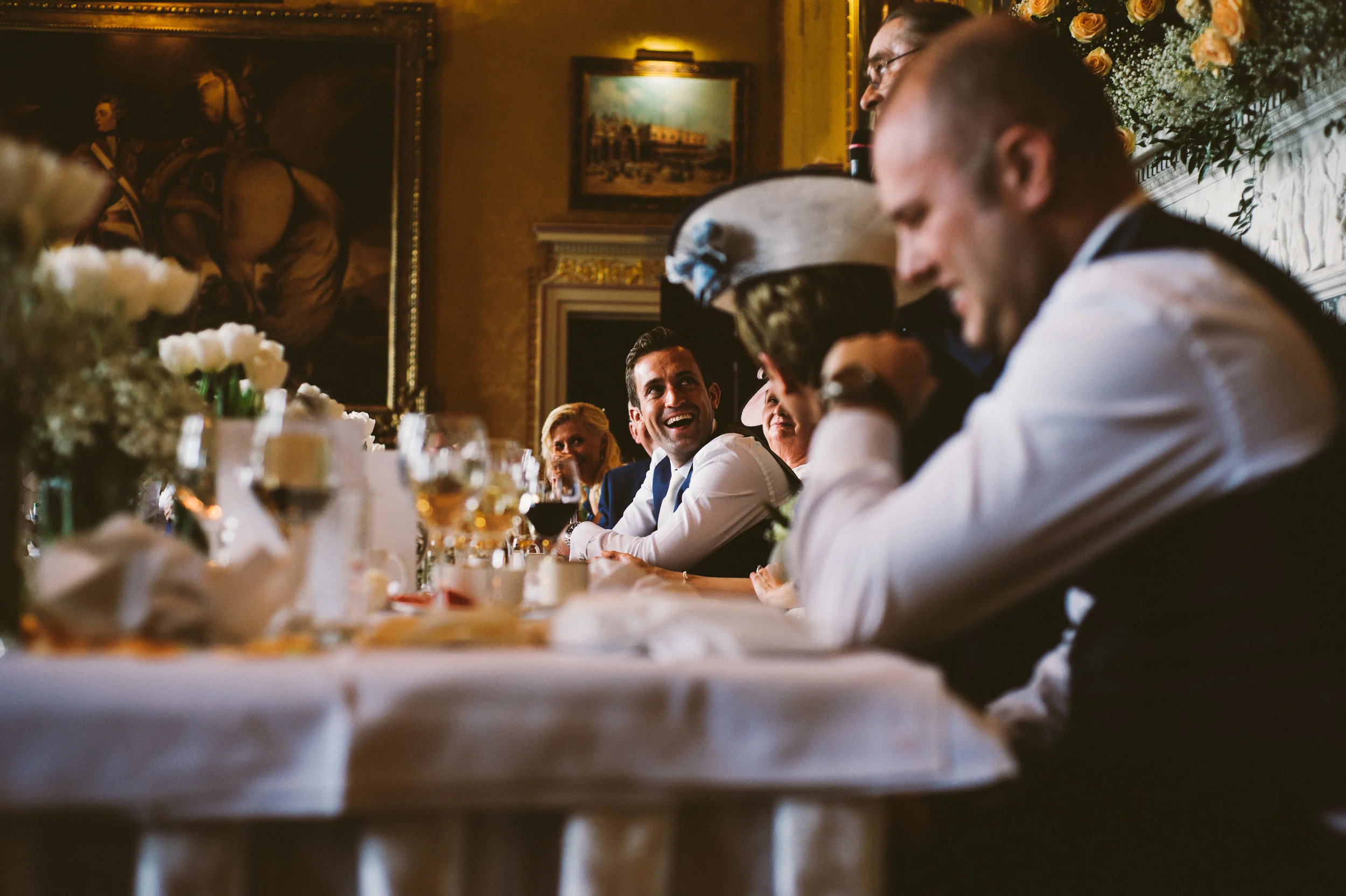 A group of people sitting at a formal dinner table in an elegant room, smiling and engaging with each other.