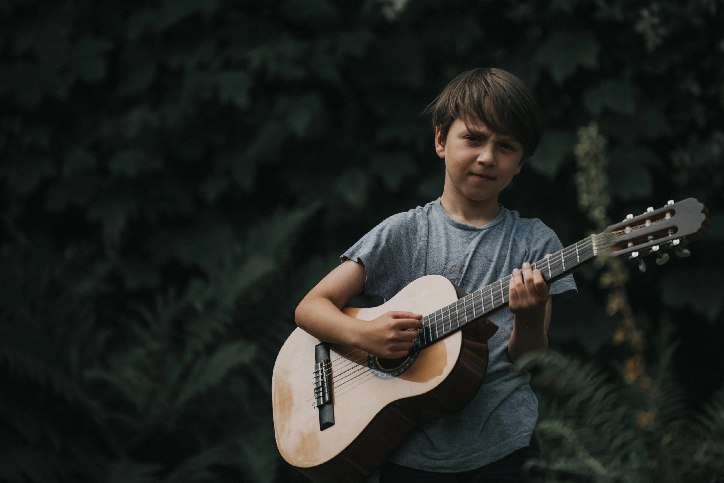 Cornwall family photographer - A young boy playing an acoustic guitar outdoors