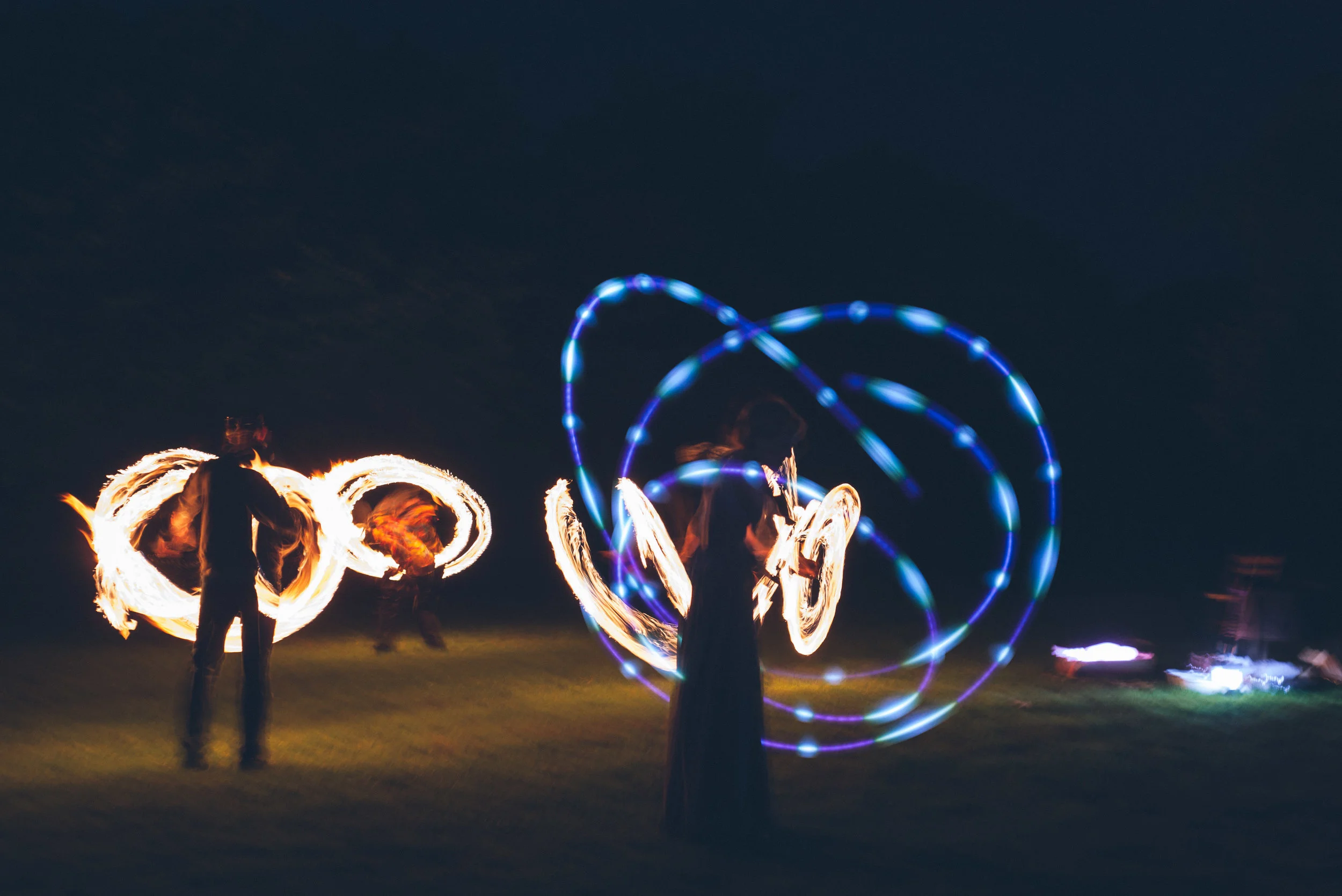 People performing fire poi and LED light twirling at night on grass.