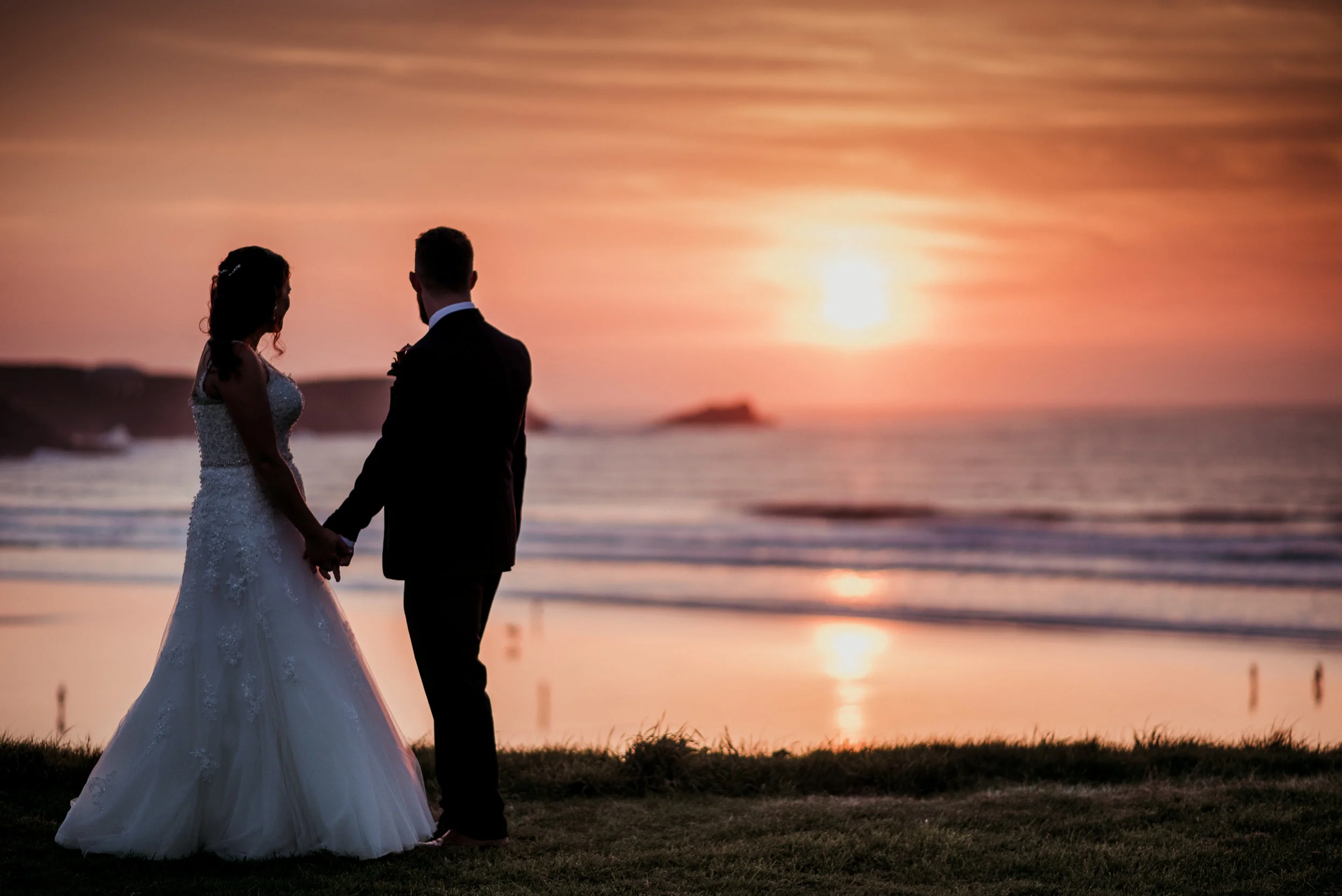 Bride and groom holding hands at sunset on a beach, captured by award-winning Cornwall wedding photographer, Mark Shaw. 