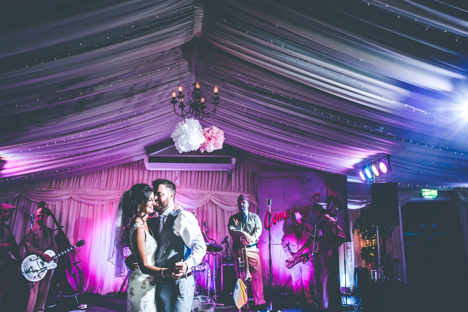Bride and groom dancing during wedding reception in a decorated marquee, with a band playing in the background, captured by award-winning Cornwall wedding photographer, Mark Shaw. 