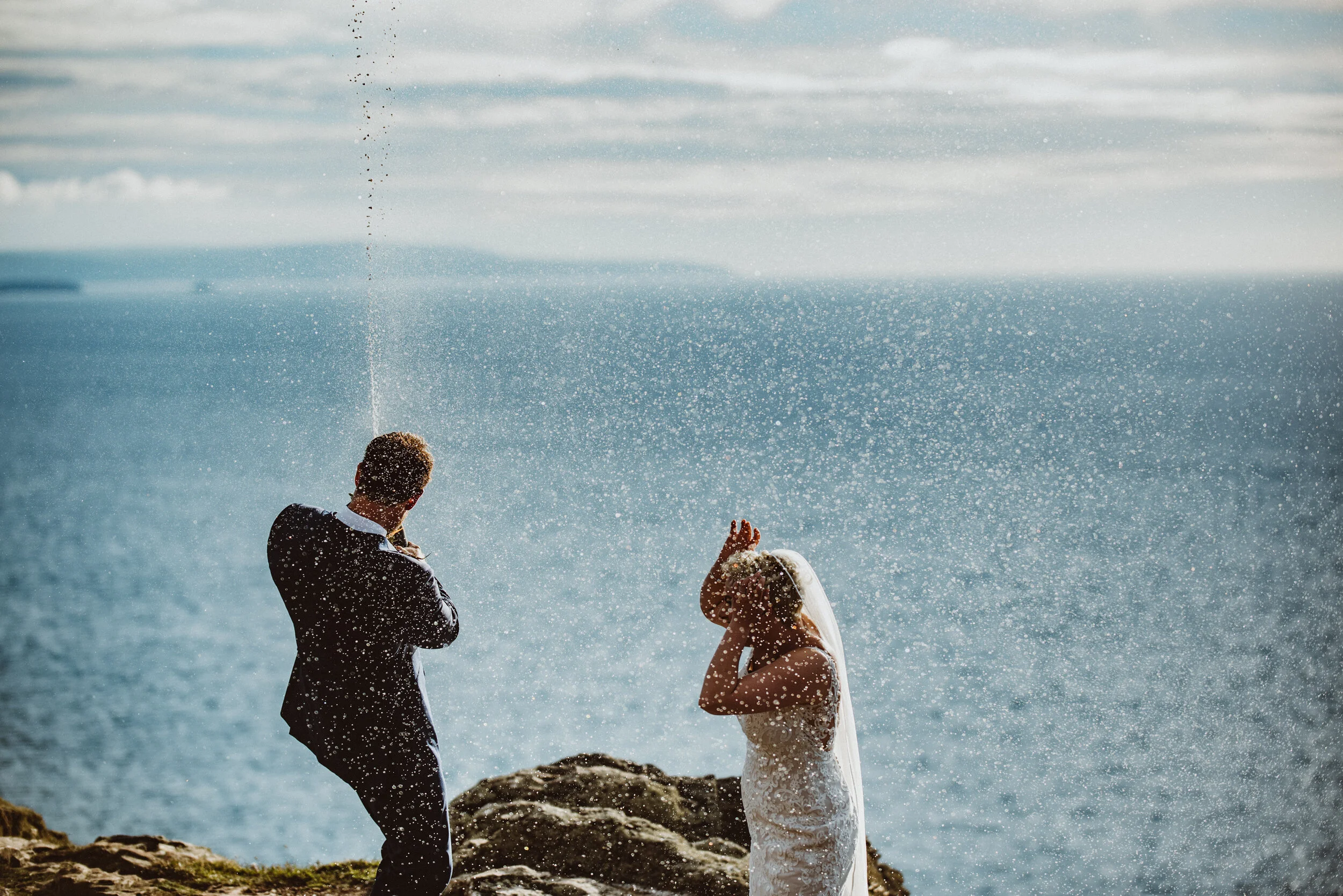 Bride and groom popping champagne on the cliffs of St Agnes Head in Cornwall captured by award-winning Cornwall wedding photographer, Mark Shaw.