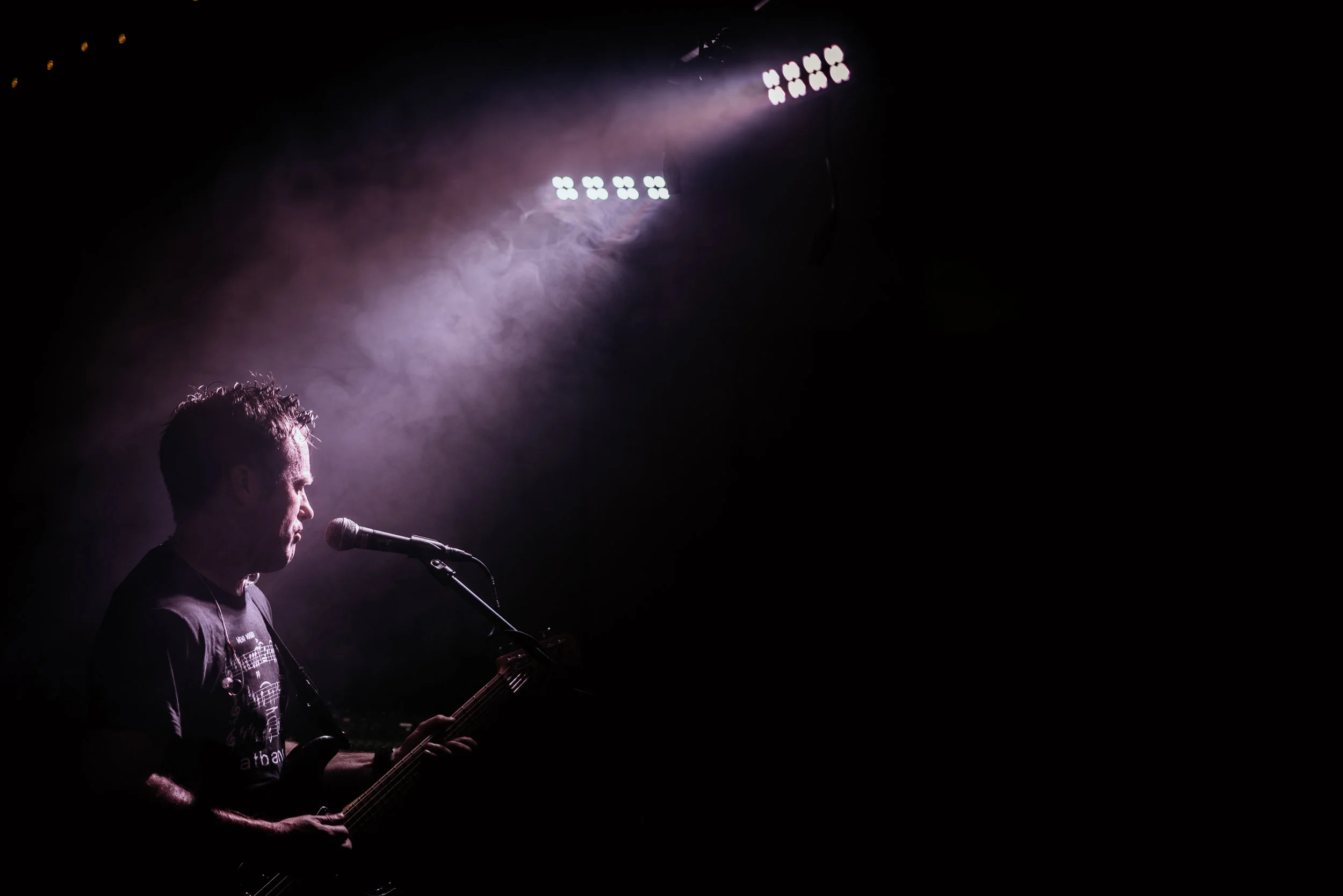 Musician playing guitar and singing on stage, with spotlight and fog effect.