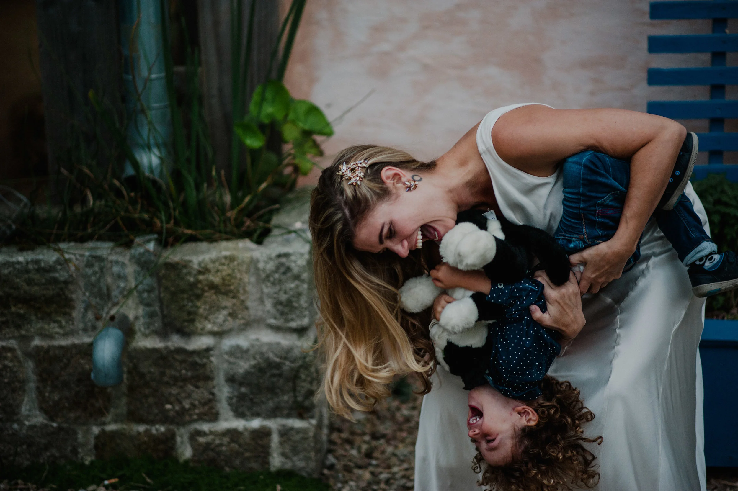 Woman playfully holding a laughing child upside down in a garden.