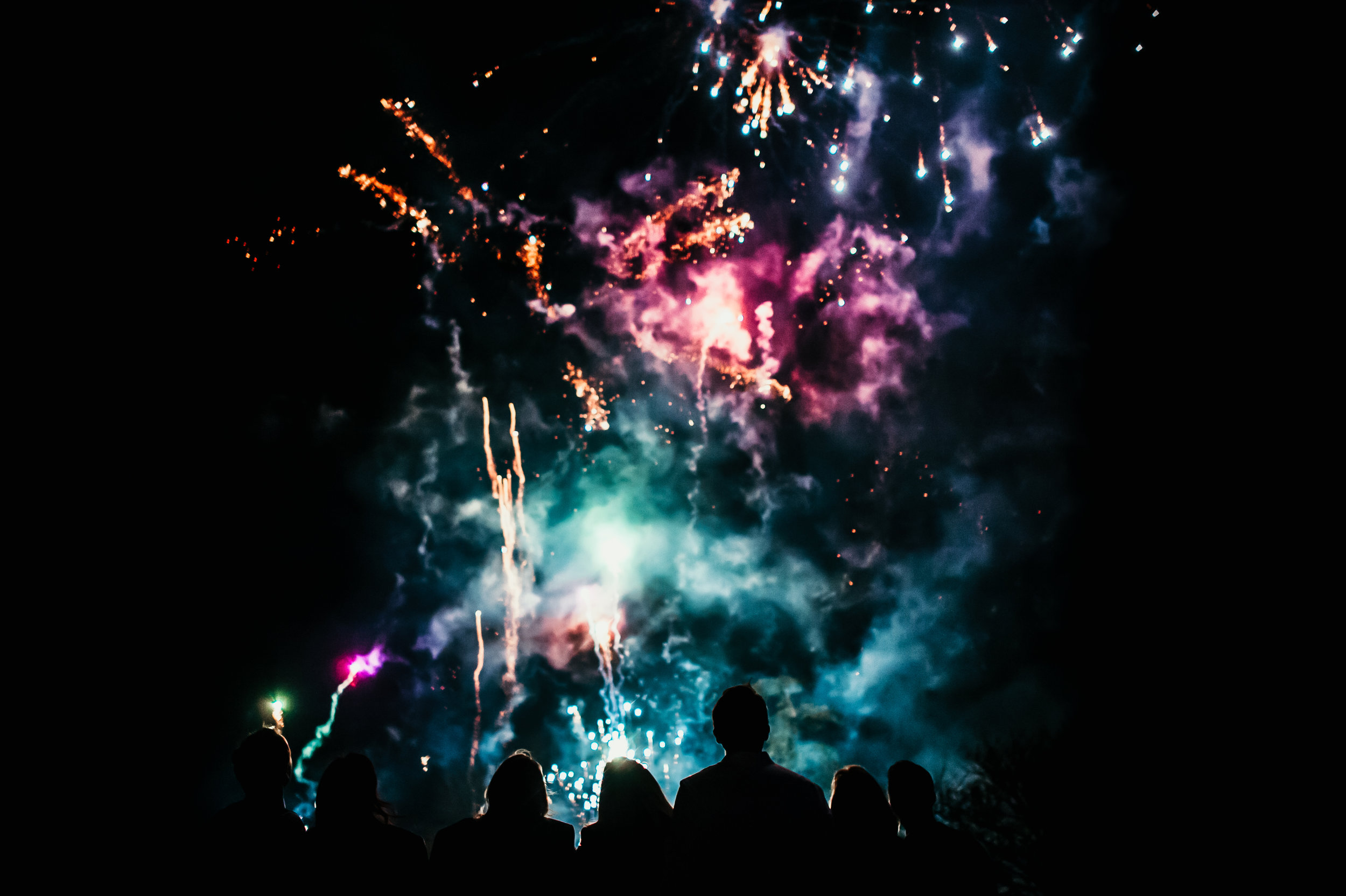 Wedding guests watching colourful fireworks at night, captured by award-winning Cornwall wedding photographer, Mark Shaw. 