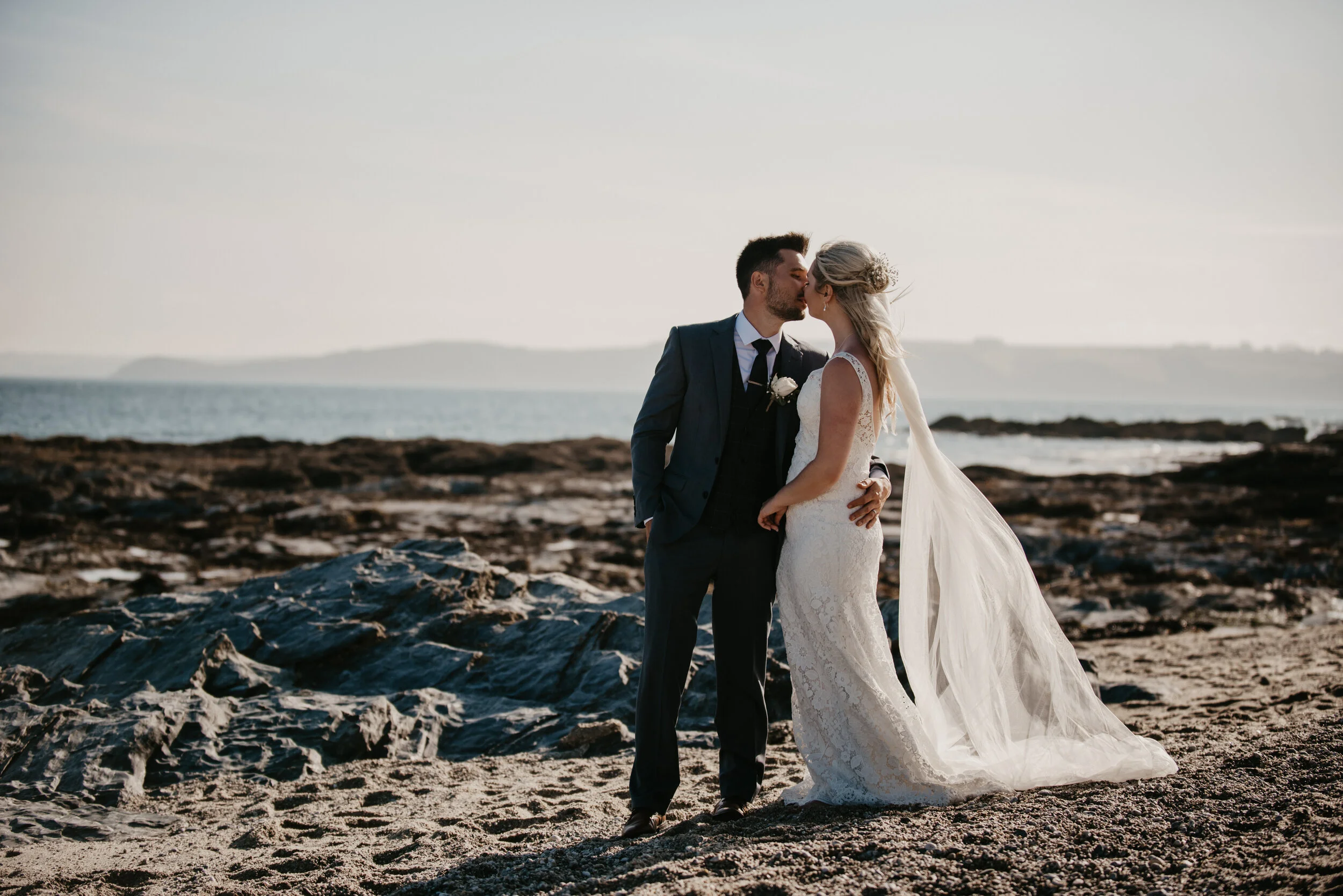 Bride and groom kissing on a rocky beach in Cornwall with the ocean in the background, captured by award-winning Cornwall wedding photographer, Mark Shaw. 