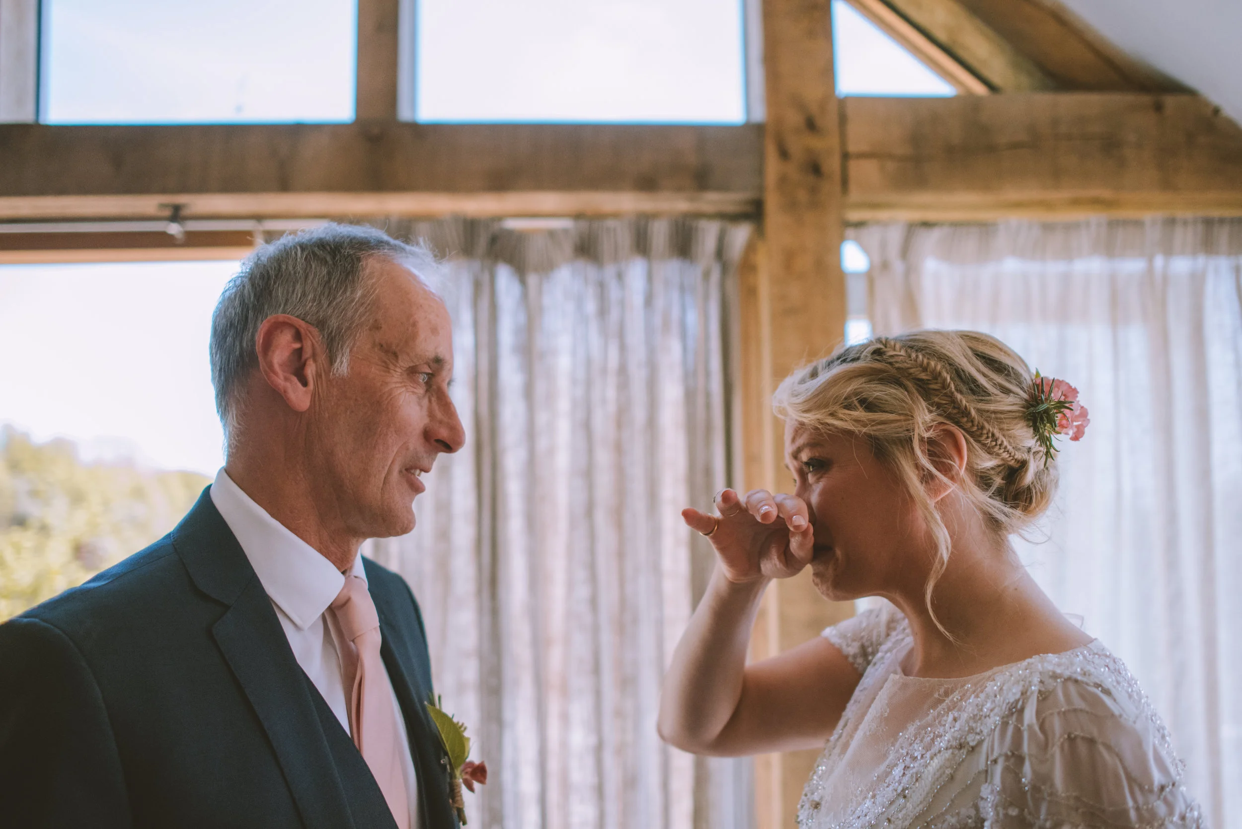 Bride and father emotional moment in wedding attire, indoor setting with natural light.