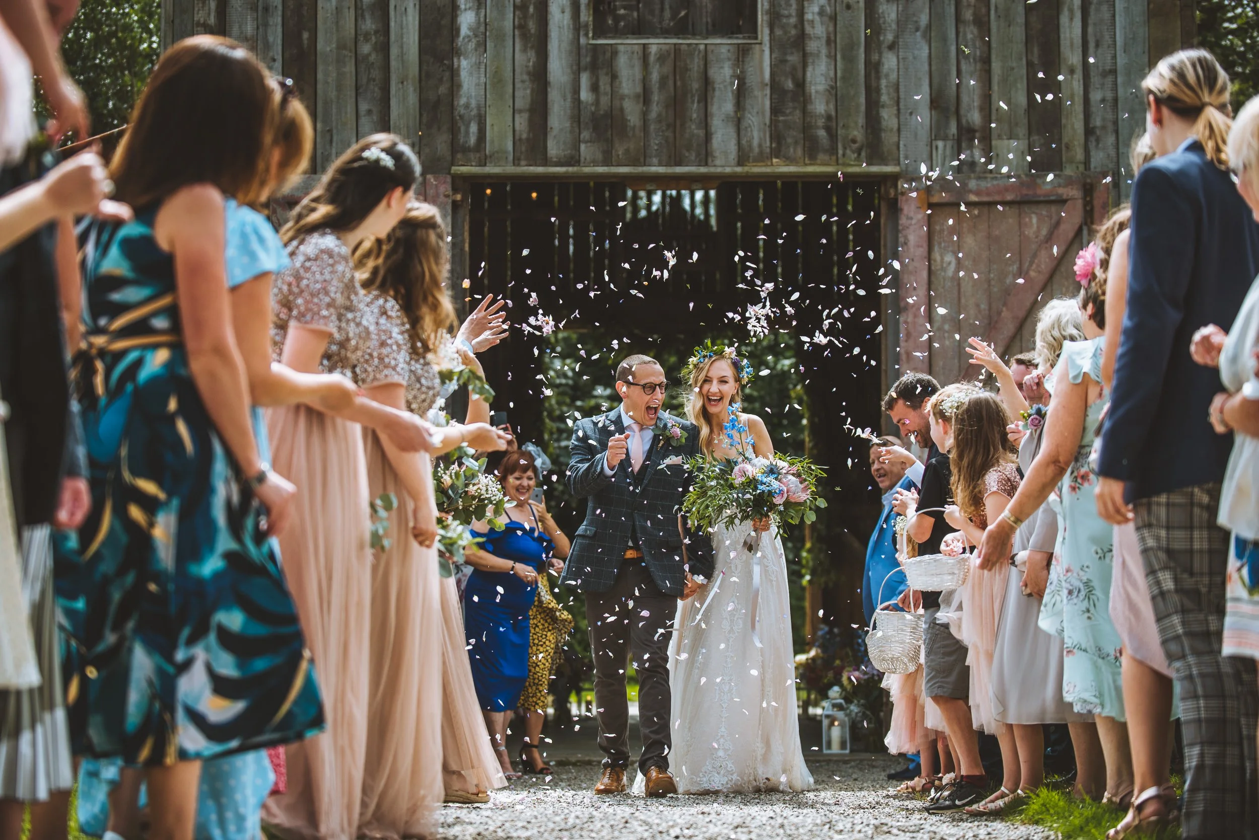 Wedding ceremony exit with guests throwing confetti at bride and groom, outdoor celebration.