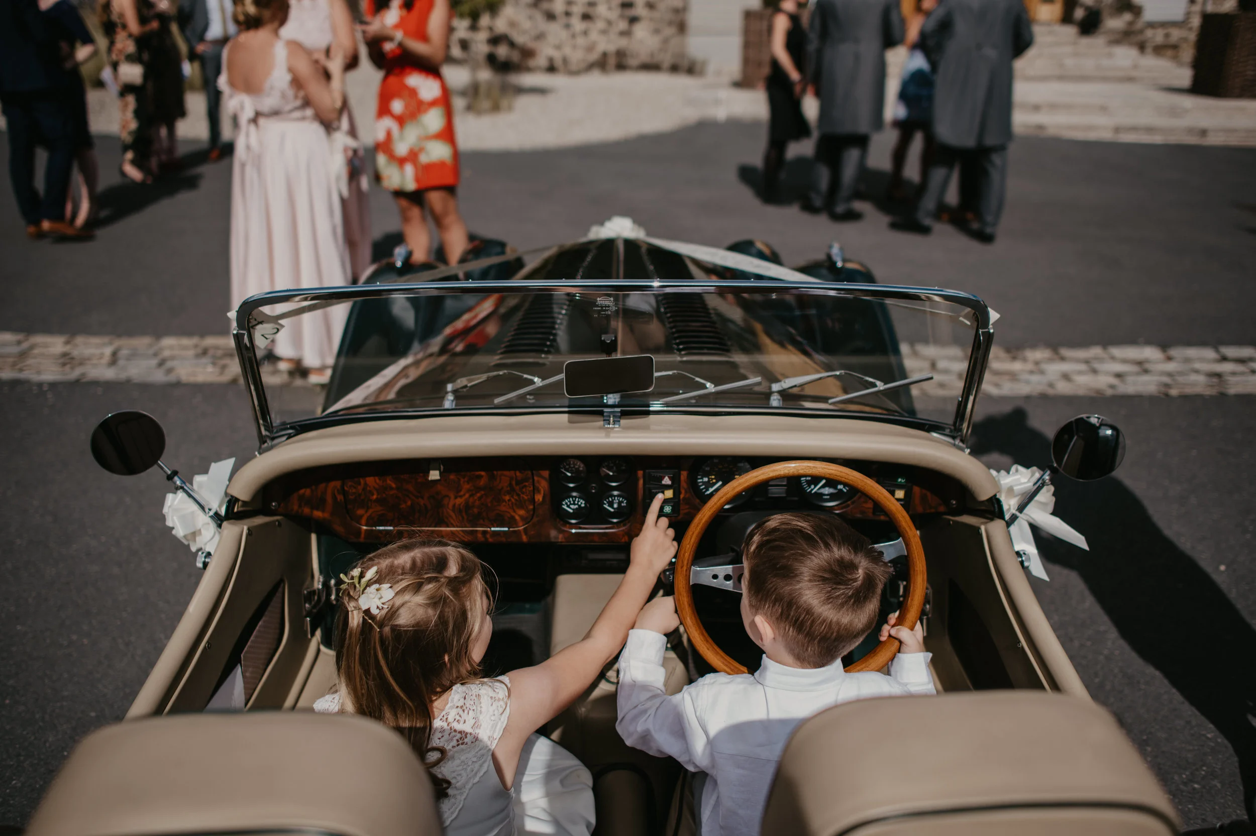 Children sitting in a vintage convertible car at a wedding, captured by award-winning Cornwall wedding photographer, Mark Shaw. 