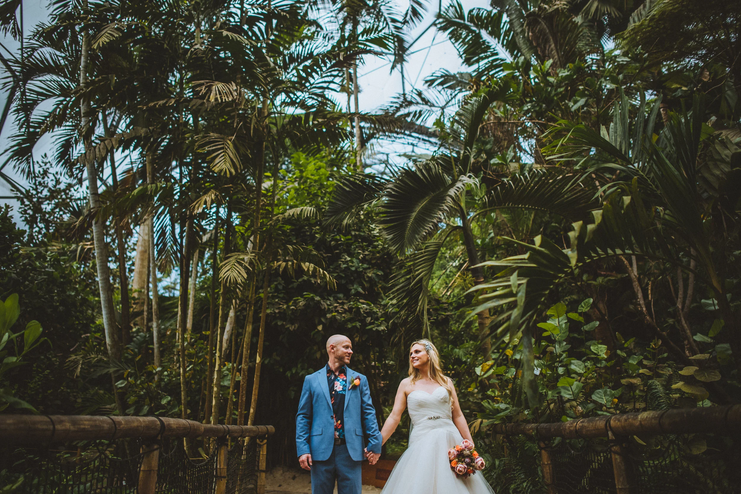 Bride and groom on a tropical path, surrounded by lush palm trees.