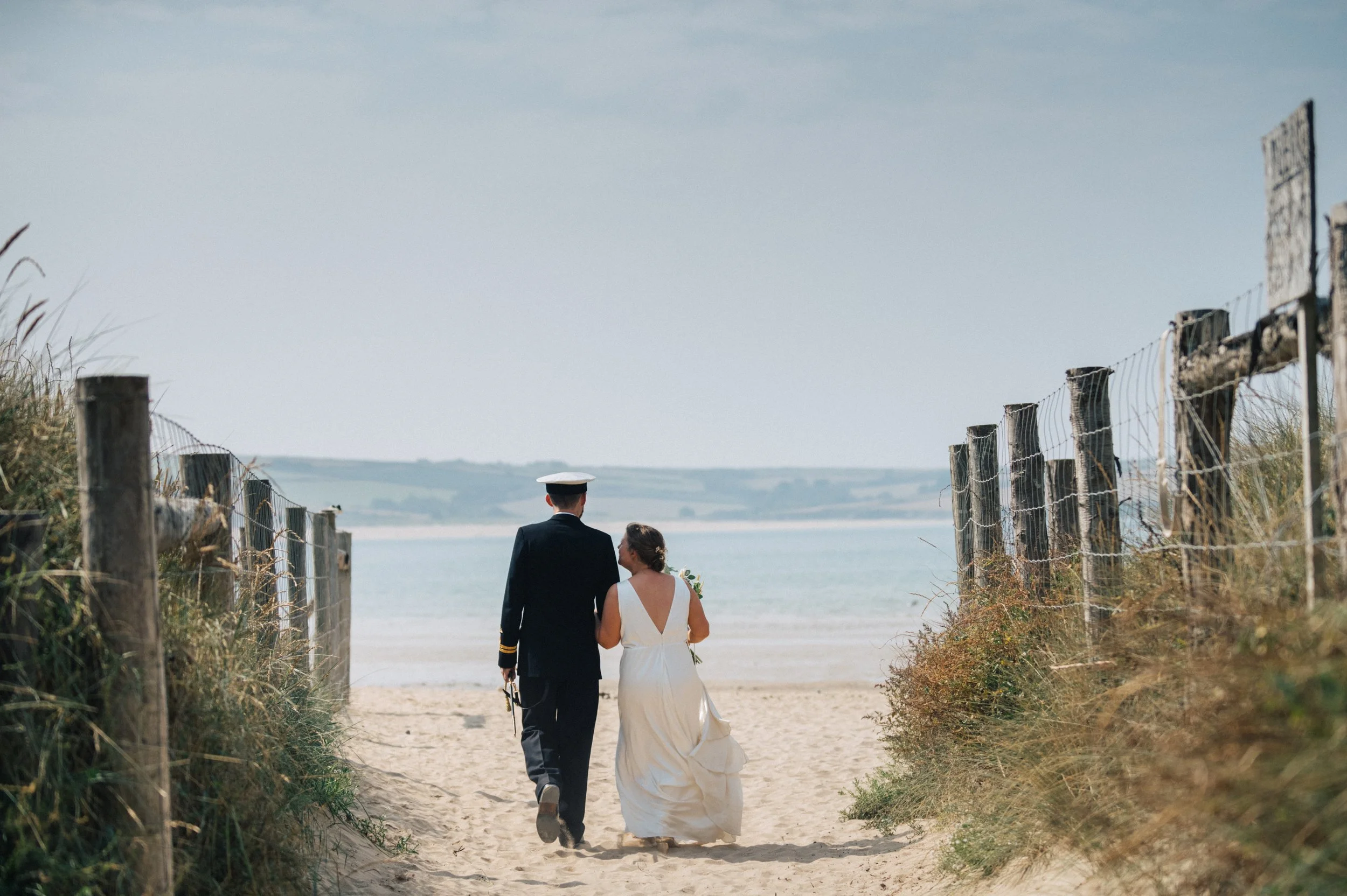 Bride and groom walking on Daymer Bay beach in Cornwall, groom dressed in military uniform, captured by award-winning Cornwall wedding photographer, Mark Shaw. 
