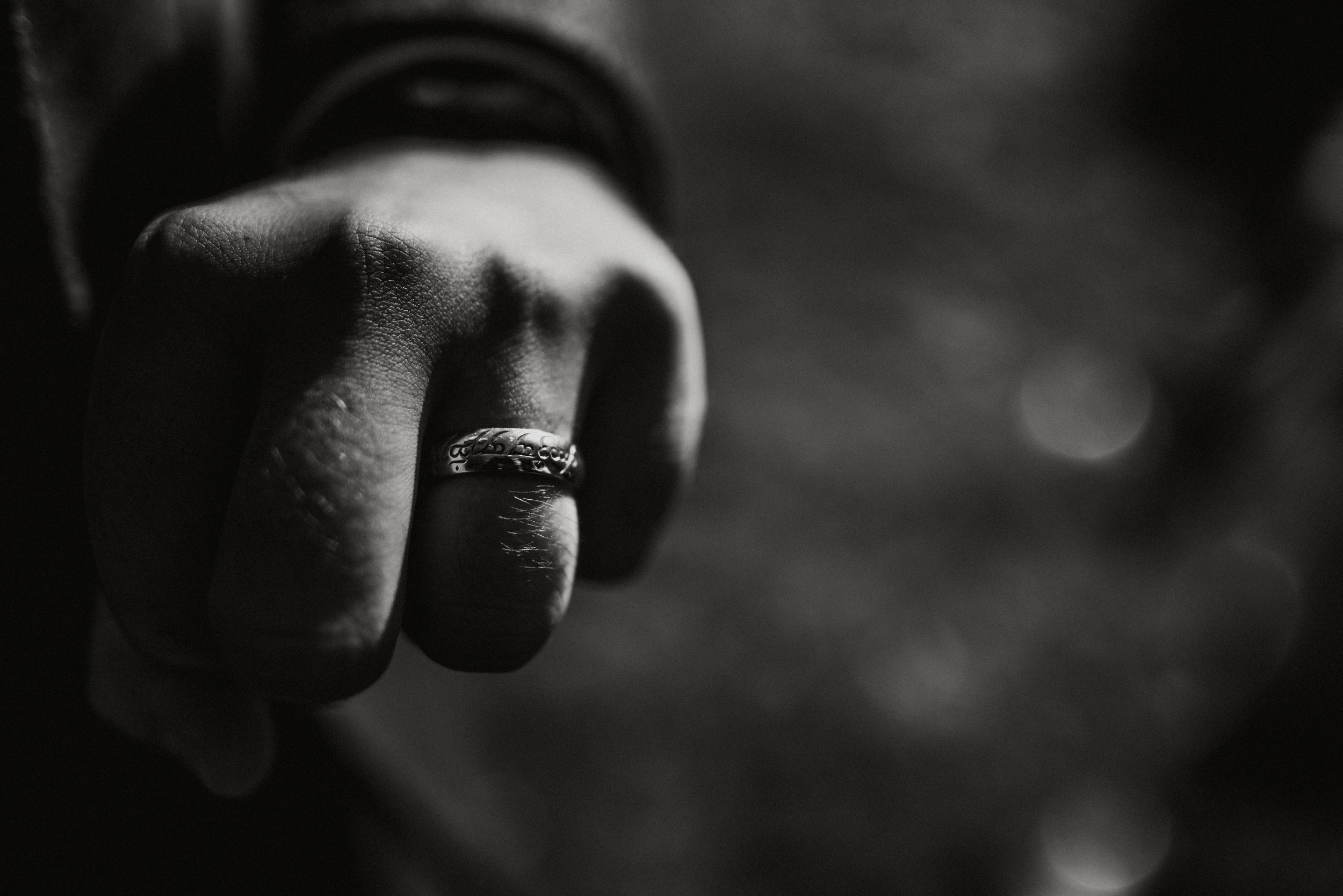 Black and white close-up of a clenched fist wearing a ring with engraved patterns, captured by award-winning Cornwall wedding photographer, Mark Shaw. 