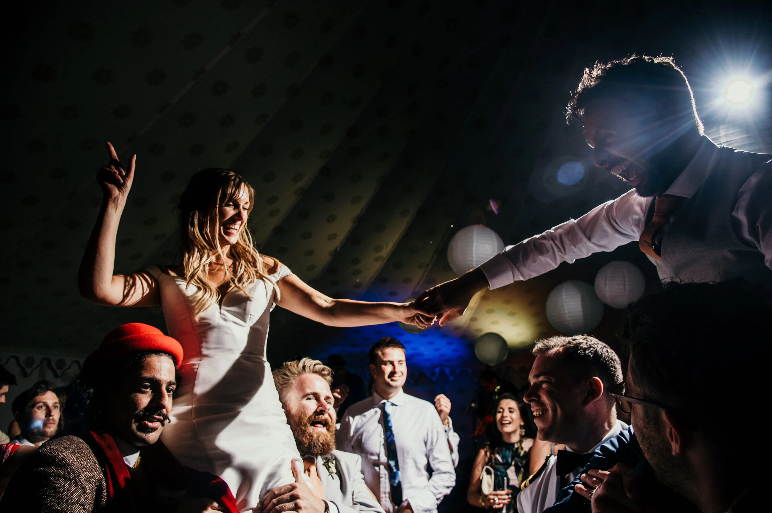 Wedding celebrations at Pencarrow House in Cornwall with bride and groom lifted by guests, festive atmosphere, people smiling and dancing.