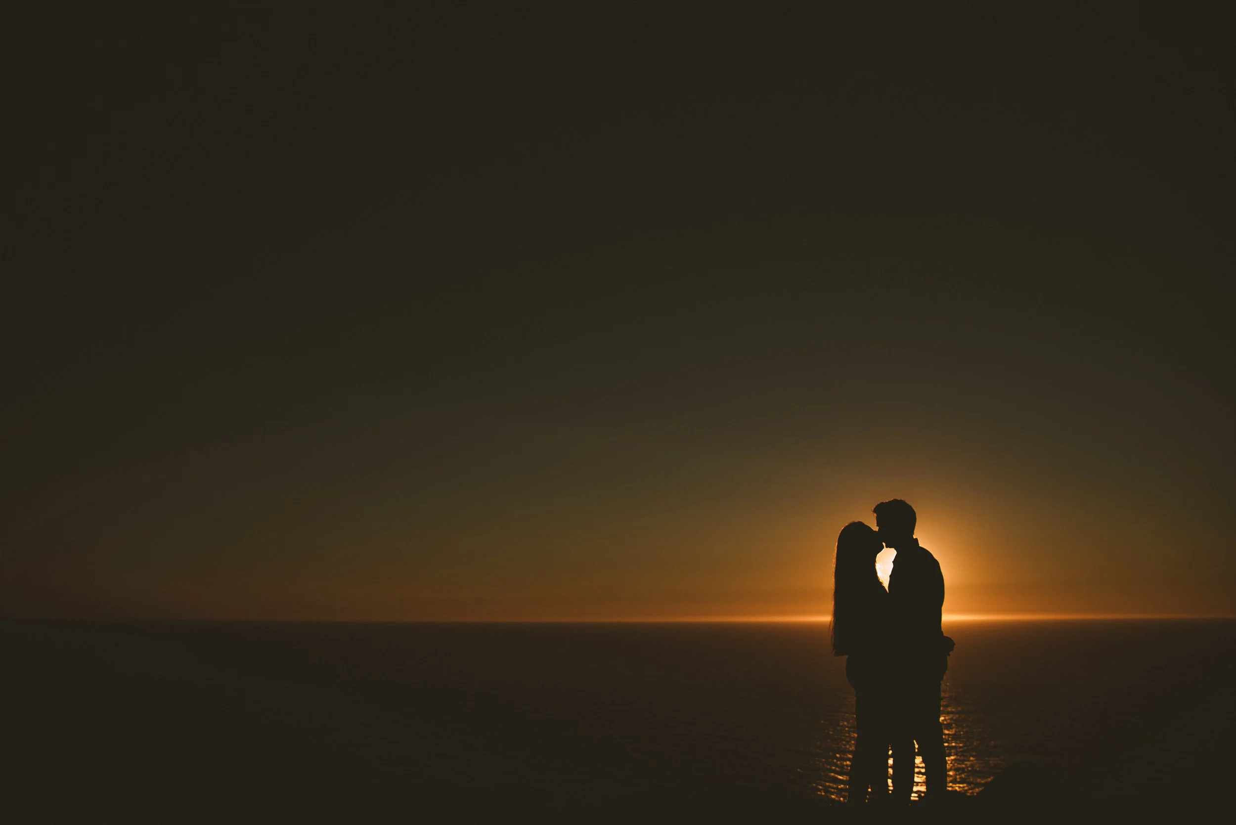 Silhouetted couple kissing at sunset over the ocean.