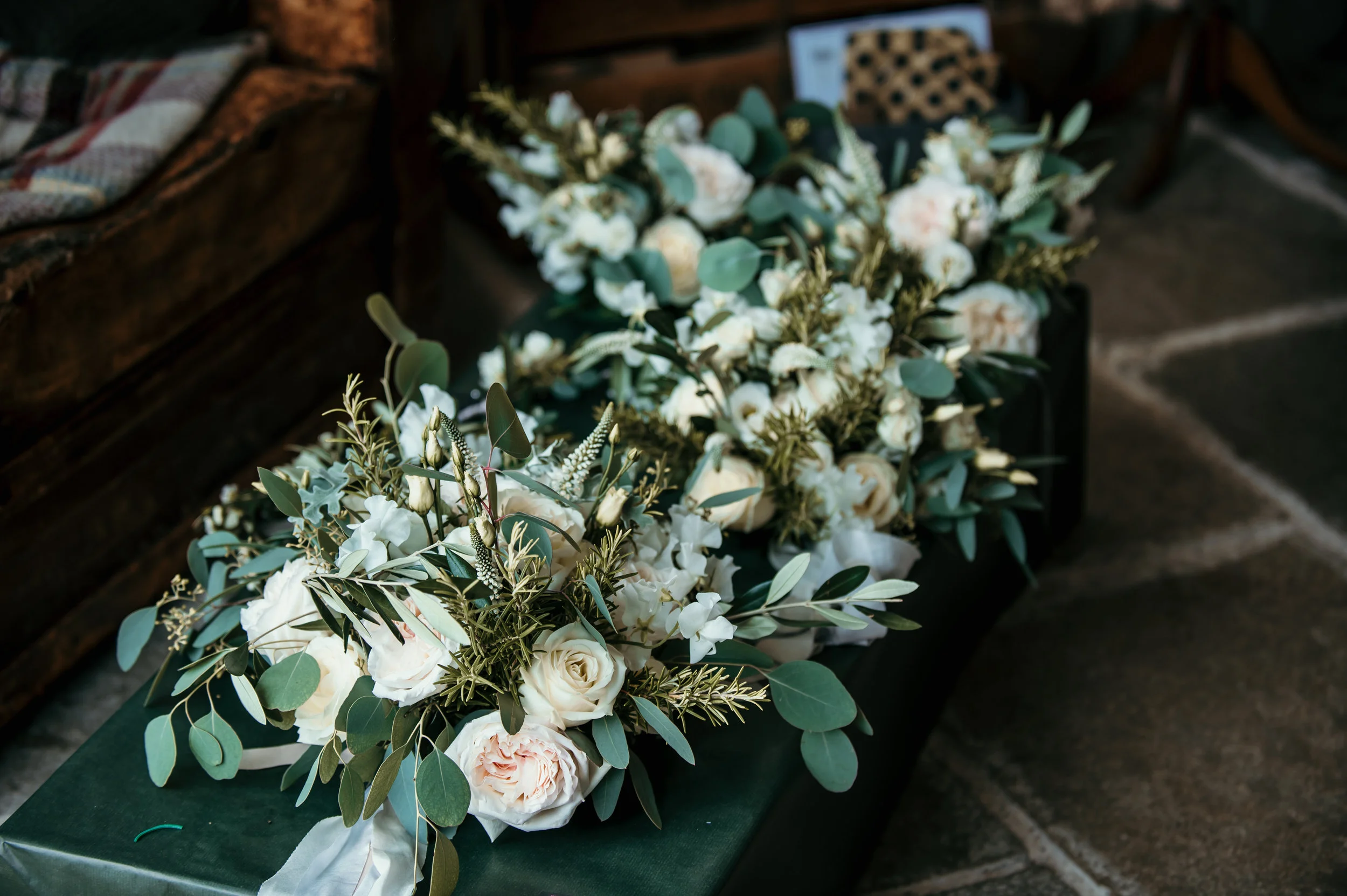 Two white floral arrangements with greenery on a dark green cloth on the floor.