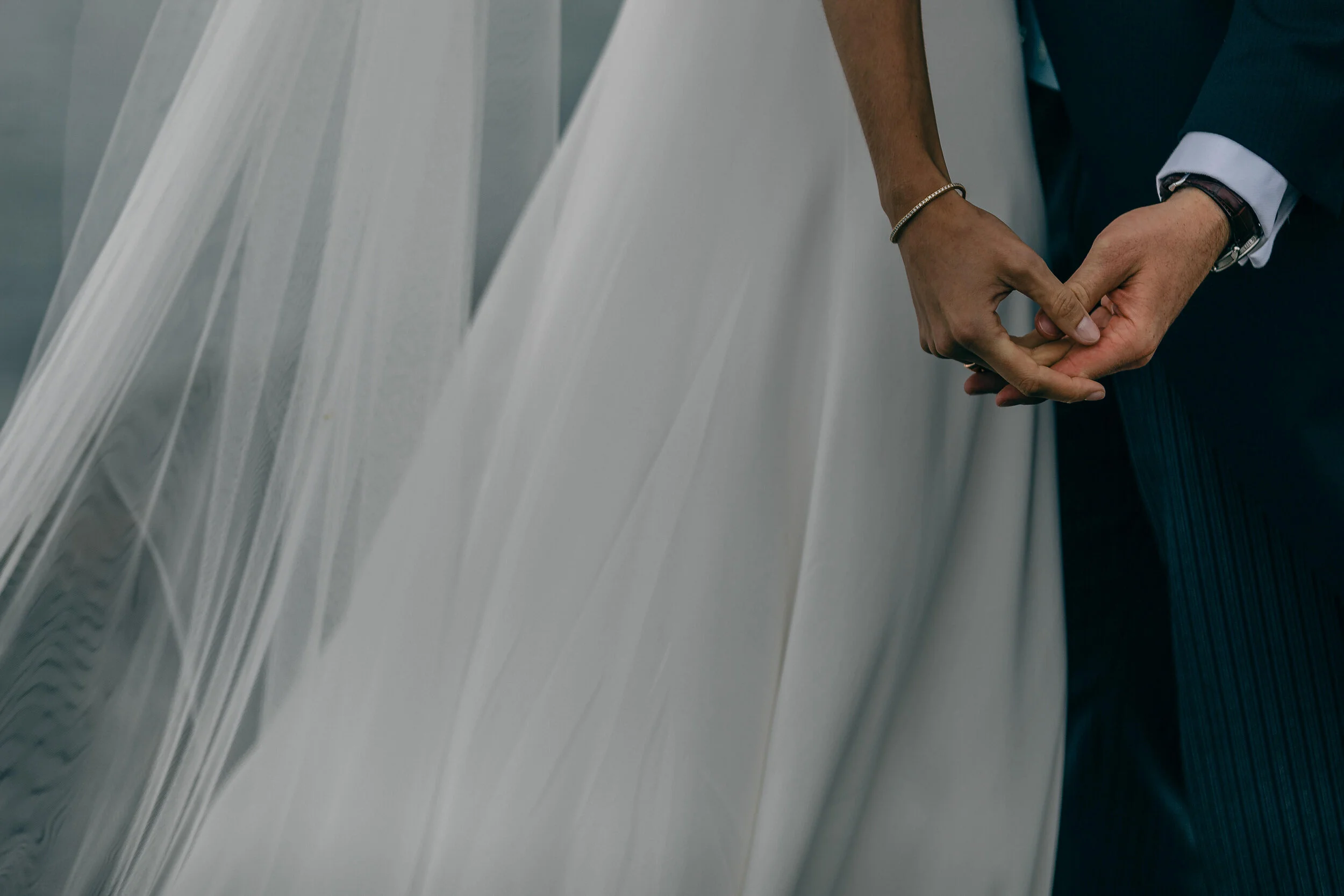 Close-up of a bride and groom holding hands during their wedding ceremony, with the bride wearing a white wedding dress and the groom in a dark suit.