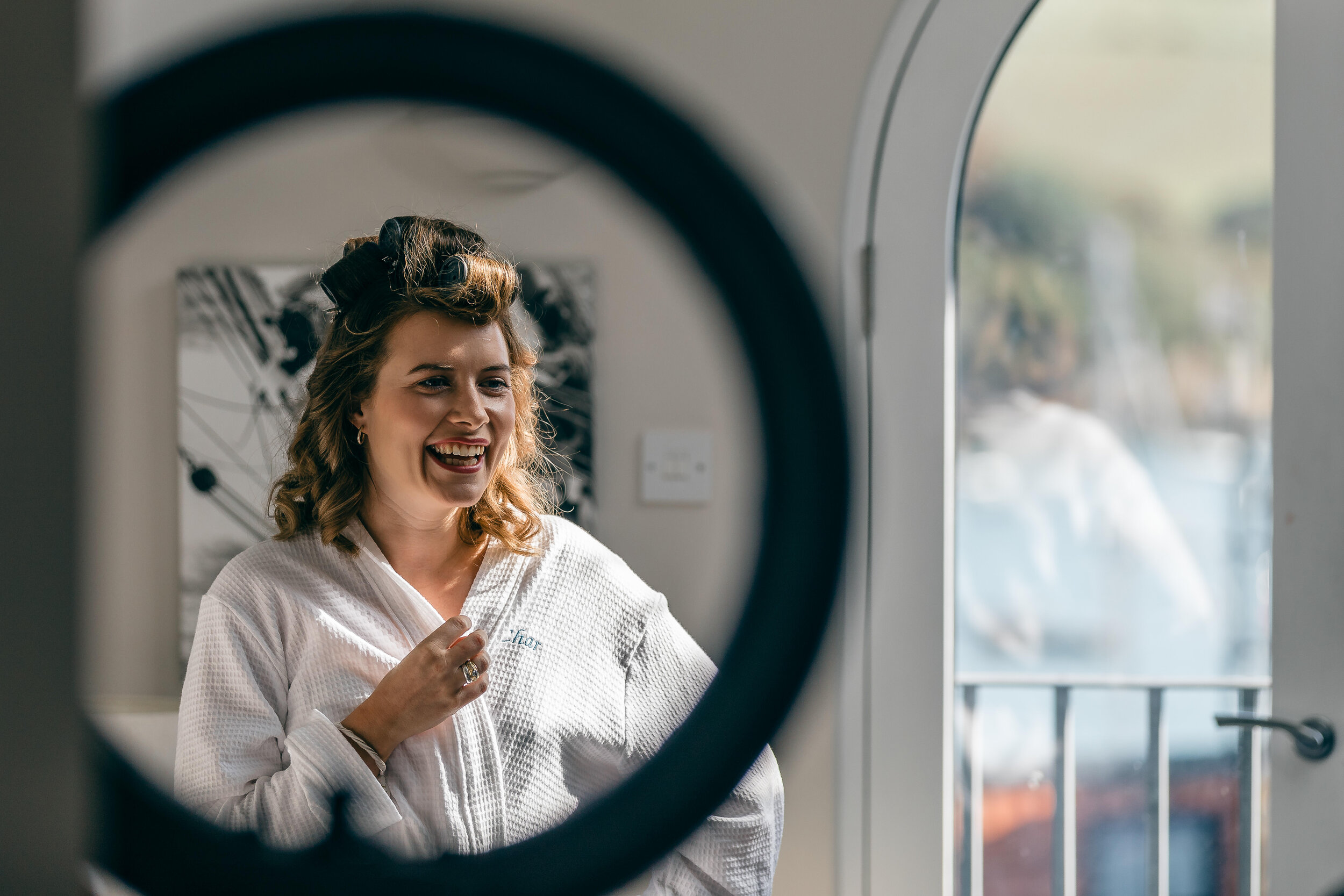 Woman smiling in front of a mirror at a salon, with her hair styled in rollers.