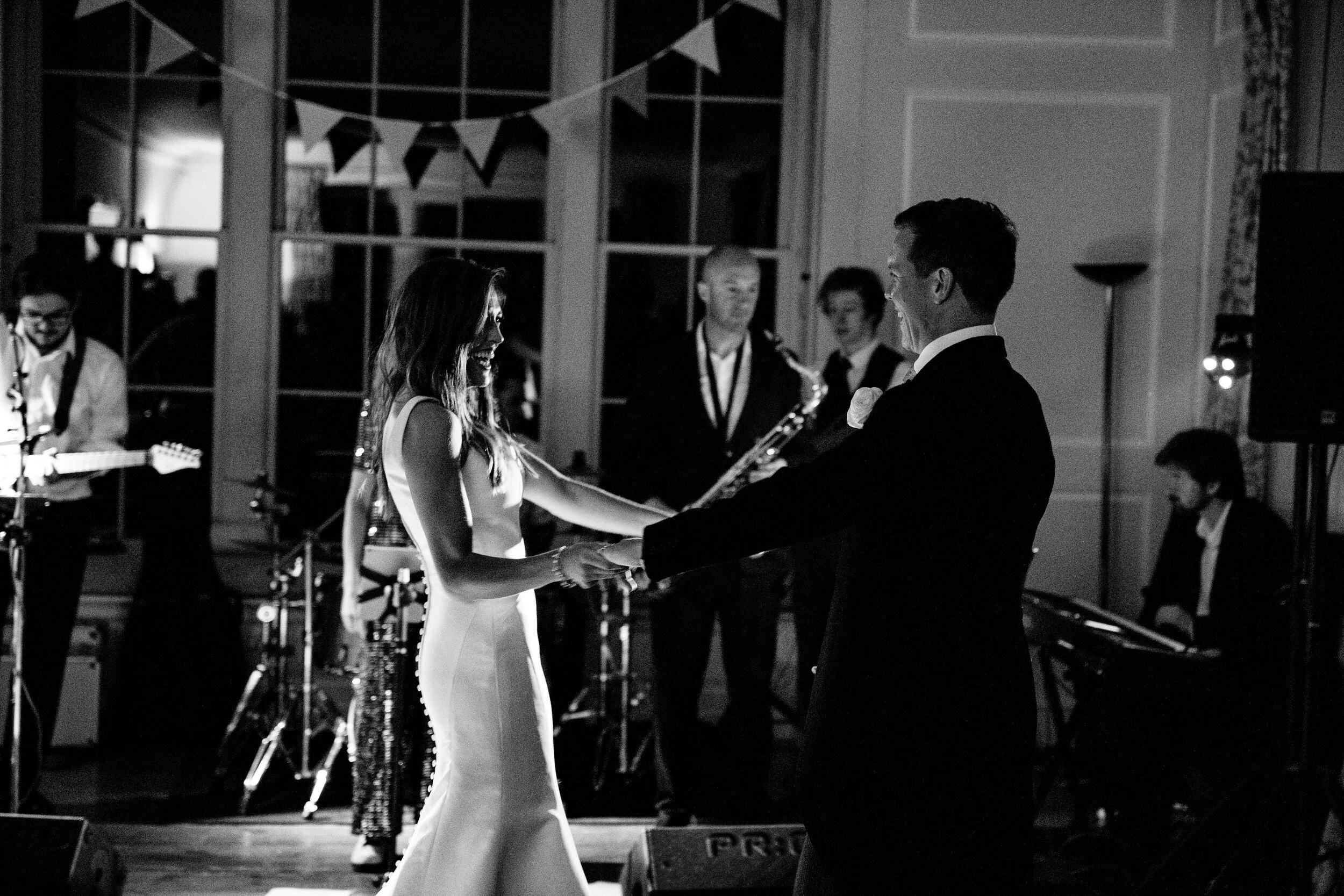 A bride and groom are dancing and smiling at their wedding reception with a band playing in the background.