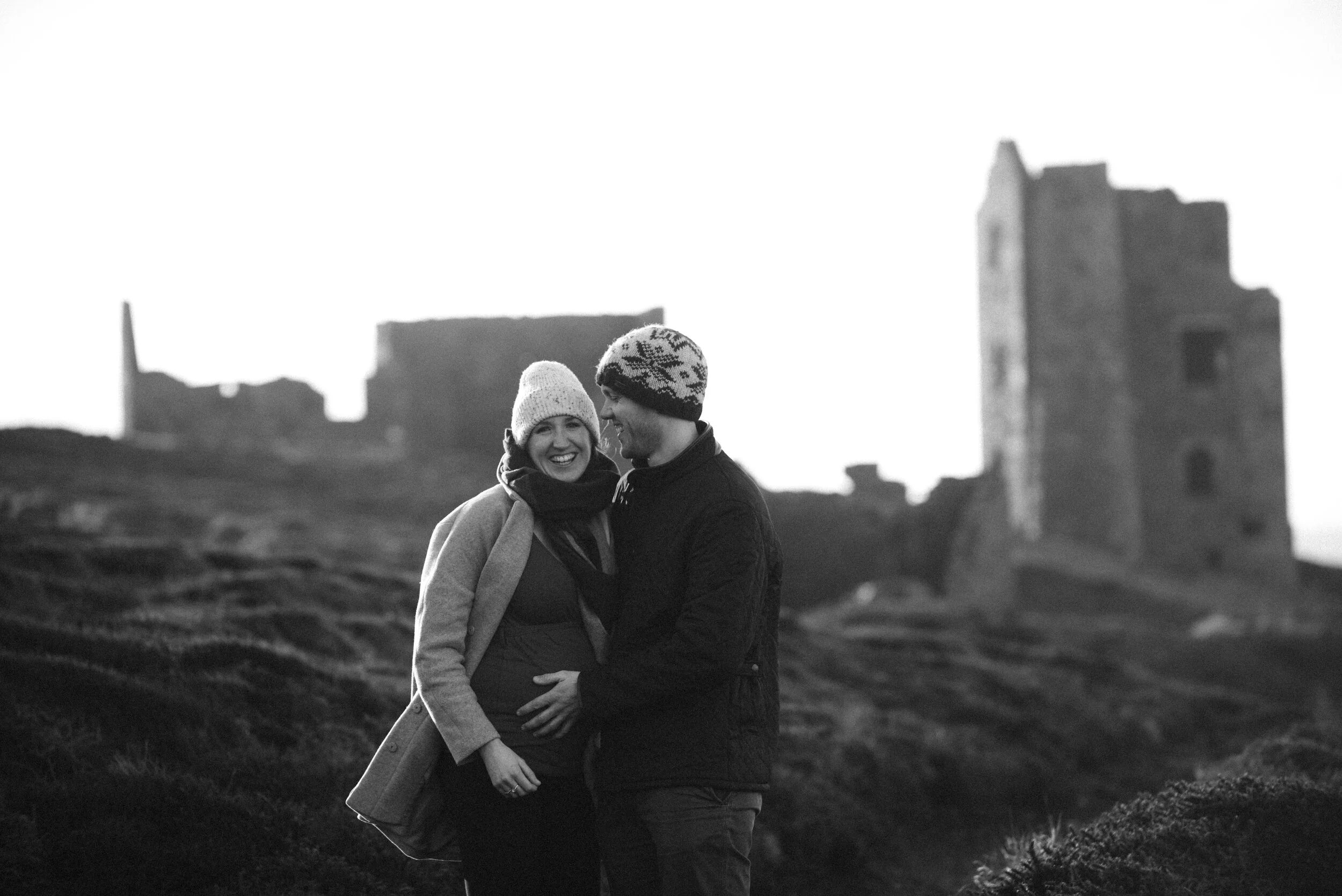 A smiling couple standing outdoors in winter clothing with ruins in the background.
