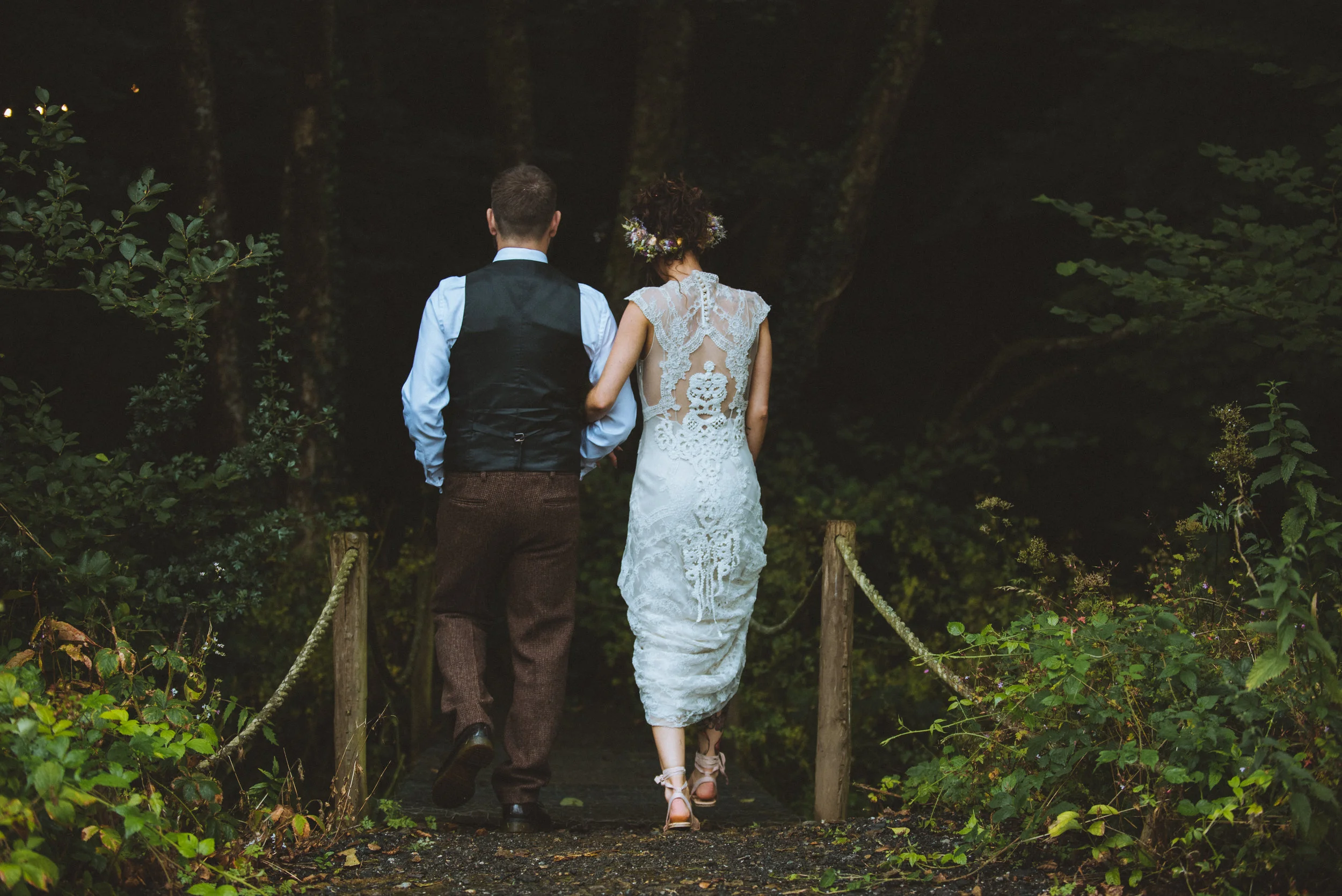 Pengenna manor wedding photography captured by Cornwall wedding photographer Mark Shaw Photography - A couple in wedding attire walking on a small path through a forest at night, with trees and greenery surrounding them.