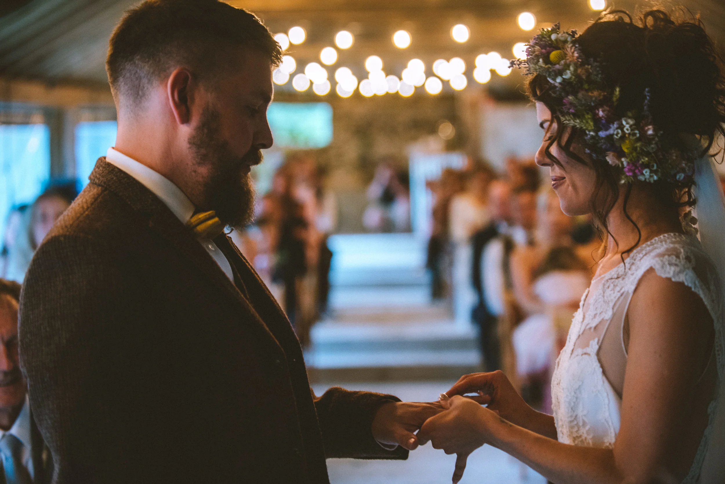 Pengenna manor wedding photography captured by Cornwall wedding photographer Mark Shaw Photography - A bride and groom exchanging vows during their wedding ceremony, holding hands, with guests watching in the background, decorated with string lights.