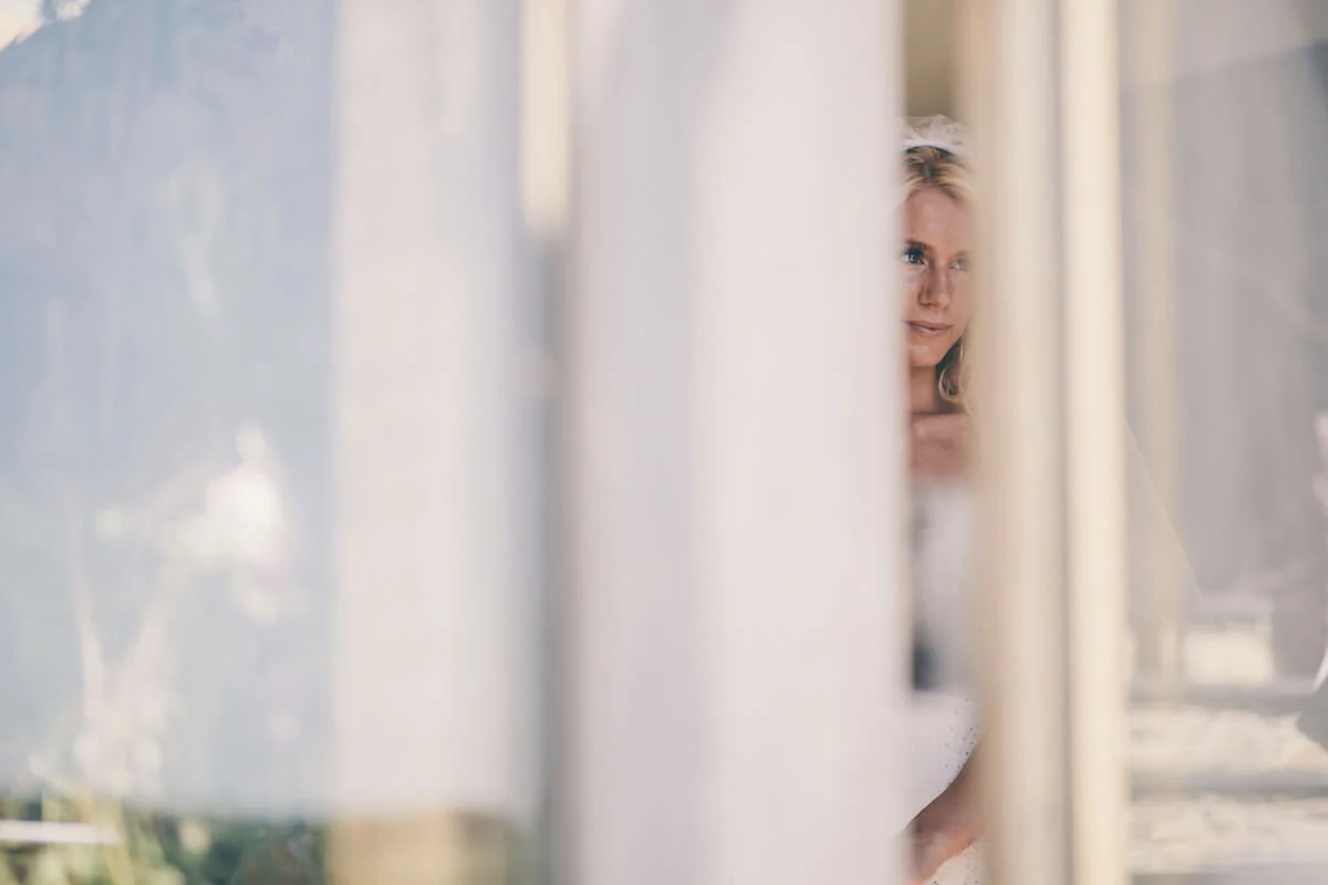 A woman with blonde hair peeking through white curtains.