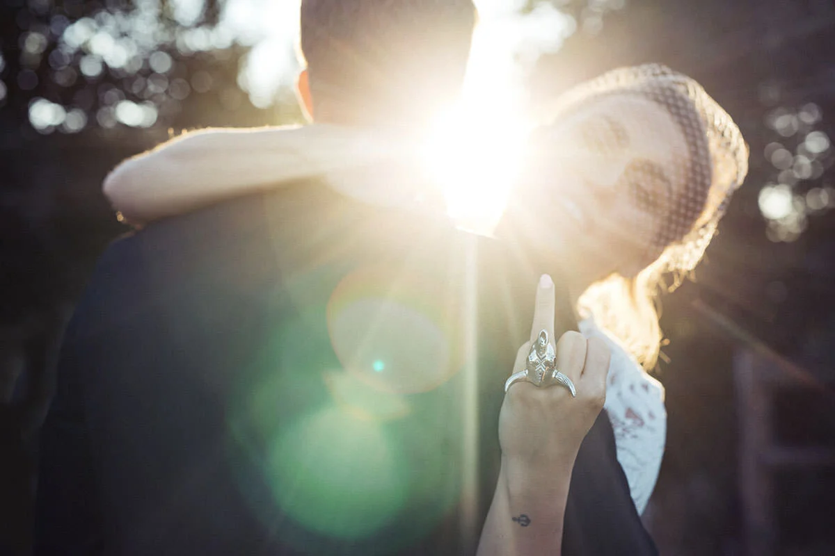 A person from behind holding a child on their shoulders outdoors during sunset, with sunlight creating a lens flare.