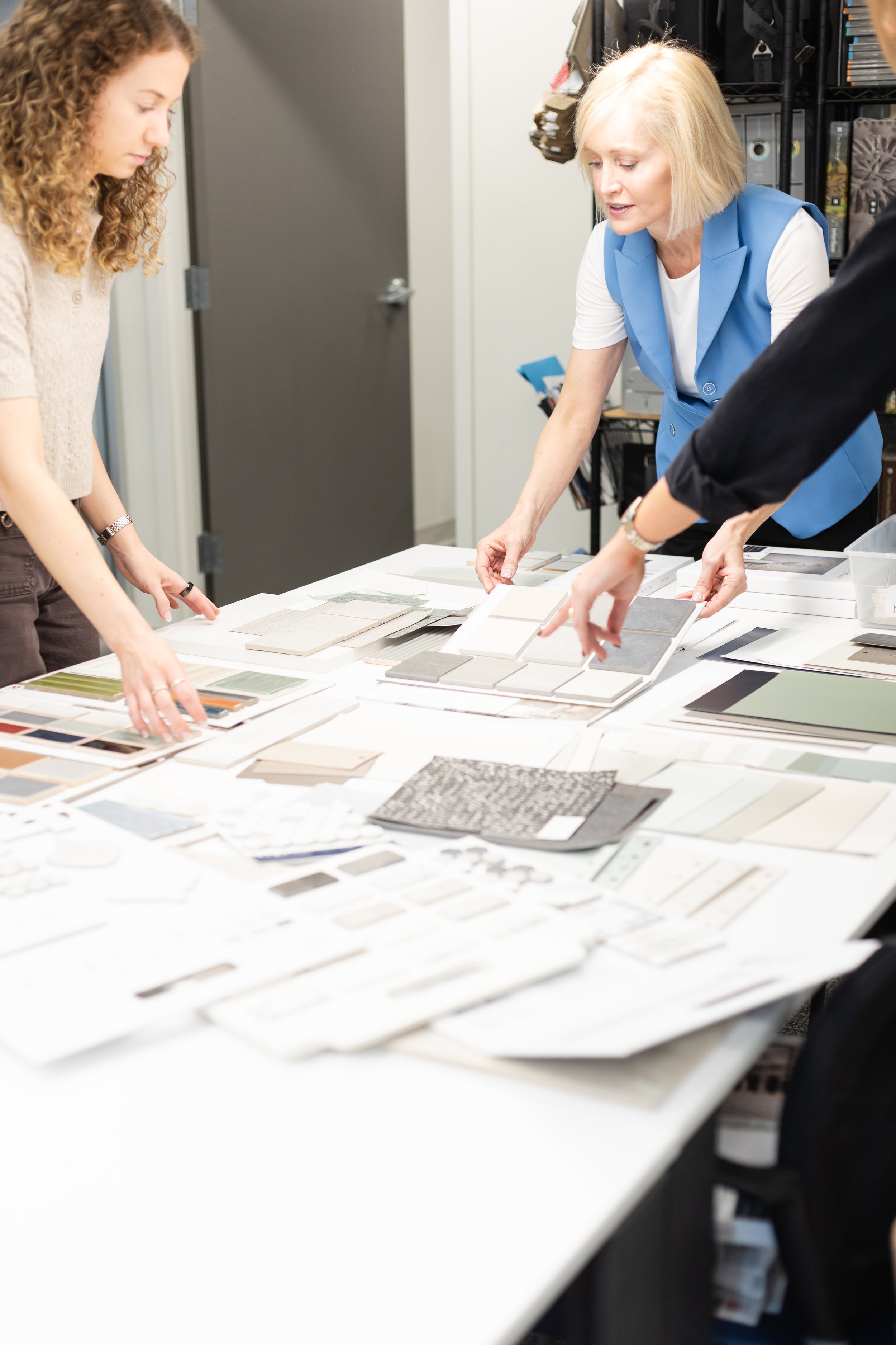 People looking at samples of fabric or material swatches spread out on a white table in a design or office setting.