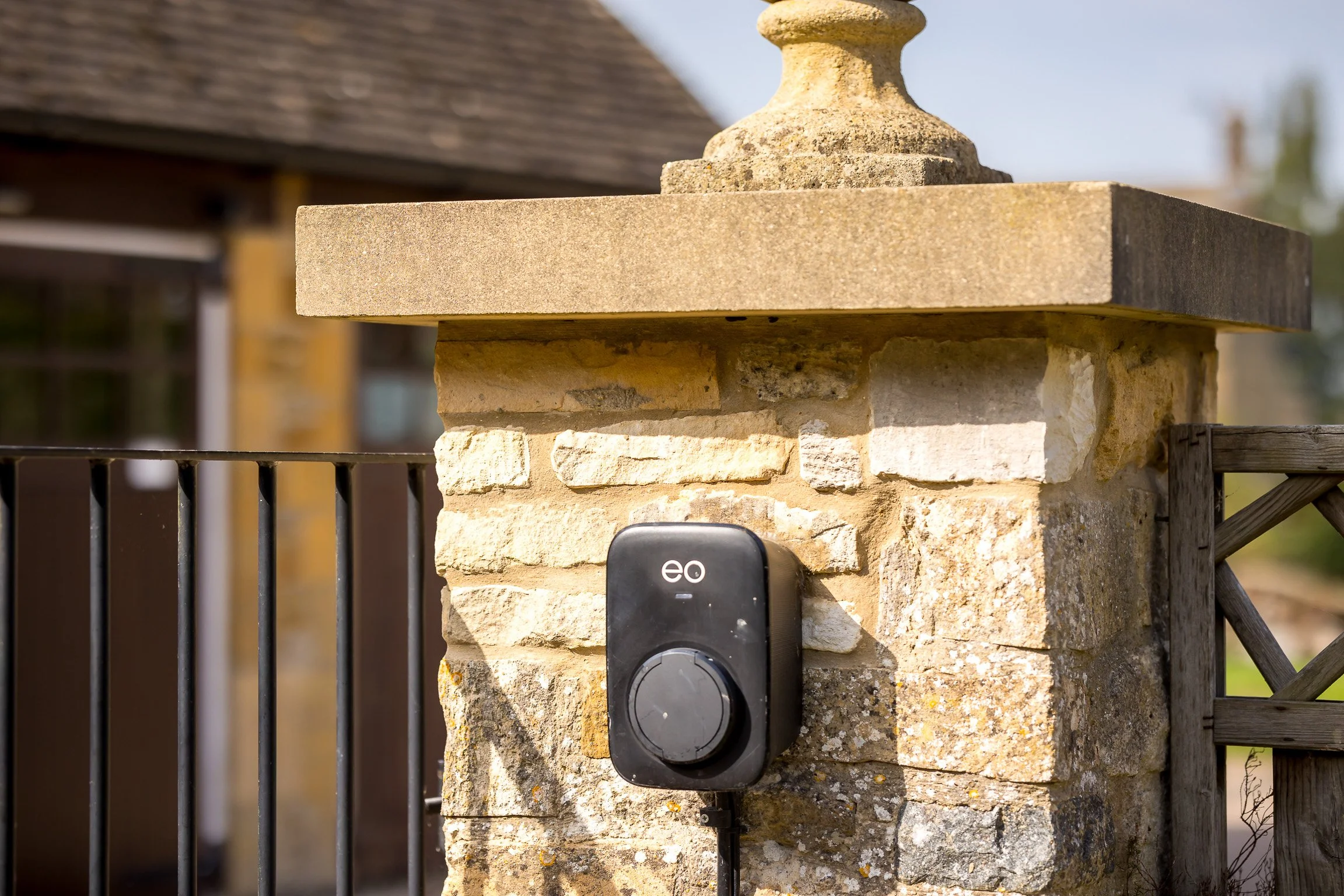 an electric vehicle charging station attached to a stone pillar on a fence outside a house during daytime
