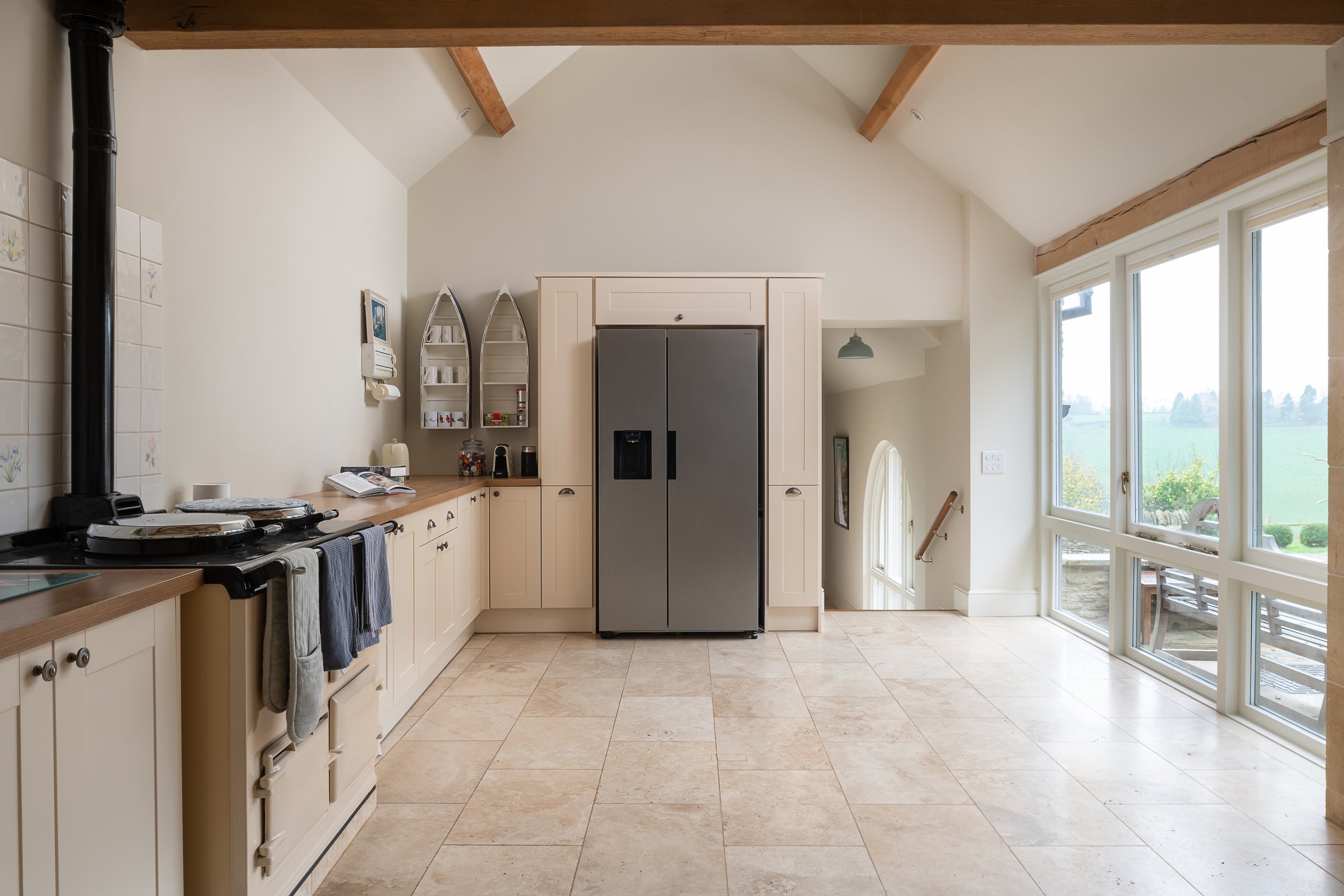 Kitchen with cream cabinets, a gray refrigerator, large windows, tiled floor, and a staircase leading downstairs.