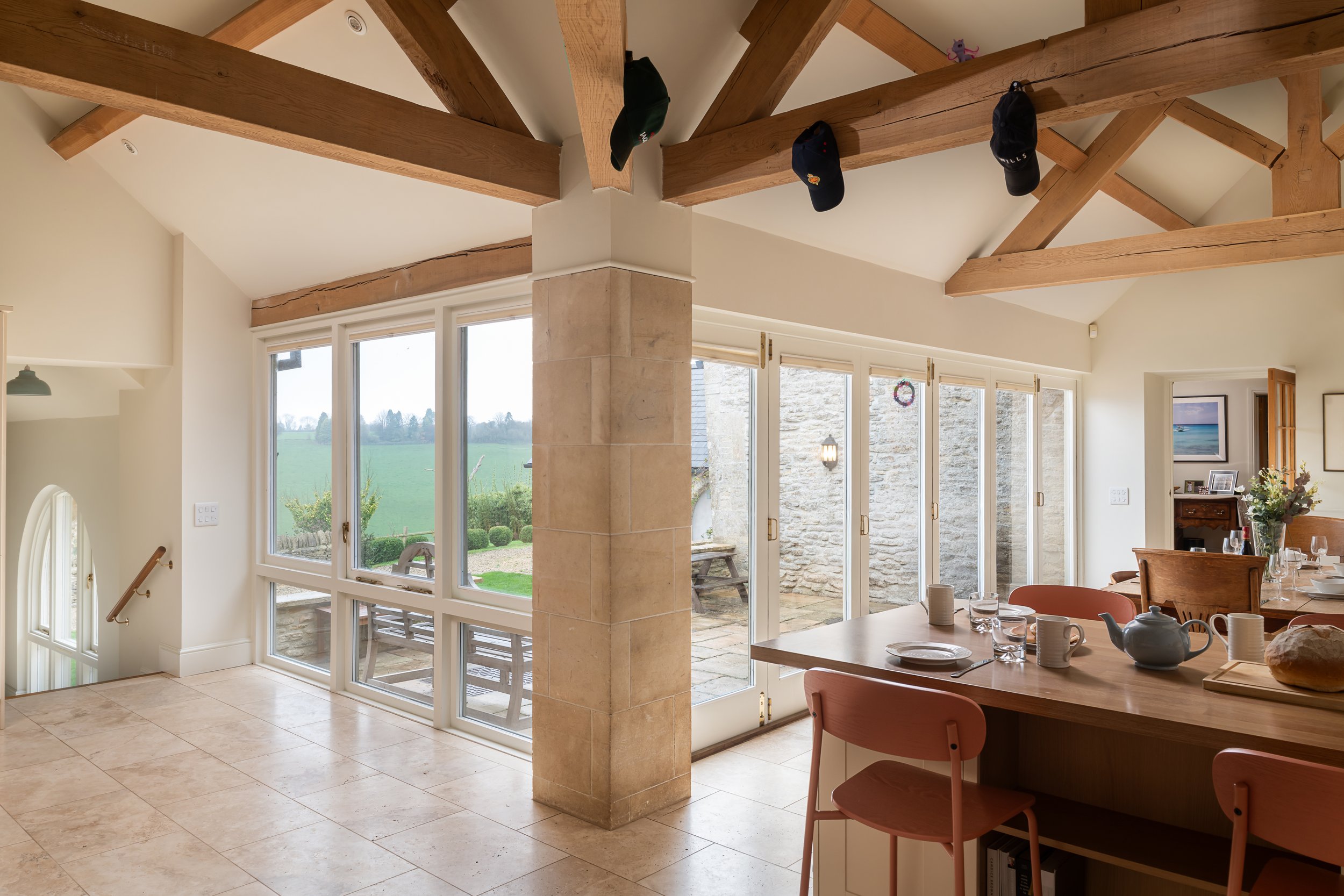 Bright dining area with large windows, wooden beams on the ceiling, and a view of a patio and green landscape outside.