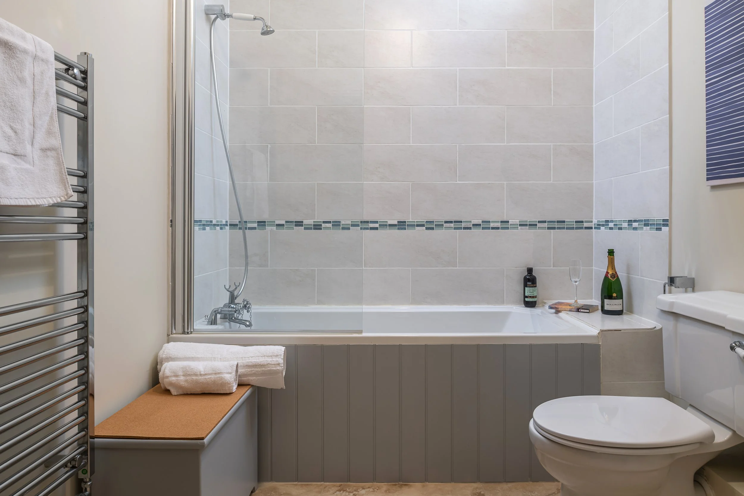 Clean bathroom with bathtub, toilet, towel rack, and decorative bottles on ledge.