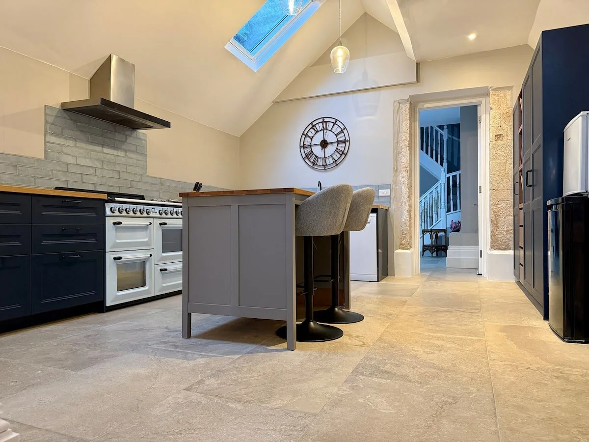 Modern kitchen with skylight, white and navy cabinets, stovetop, and kitchen island with two chairs.