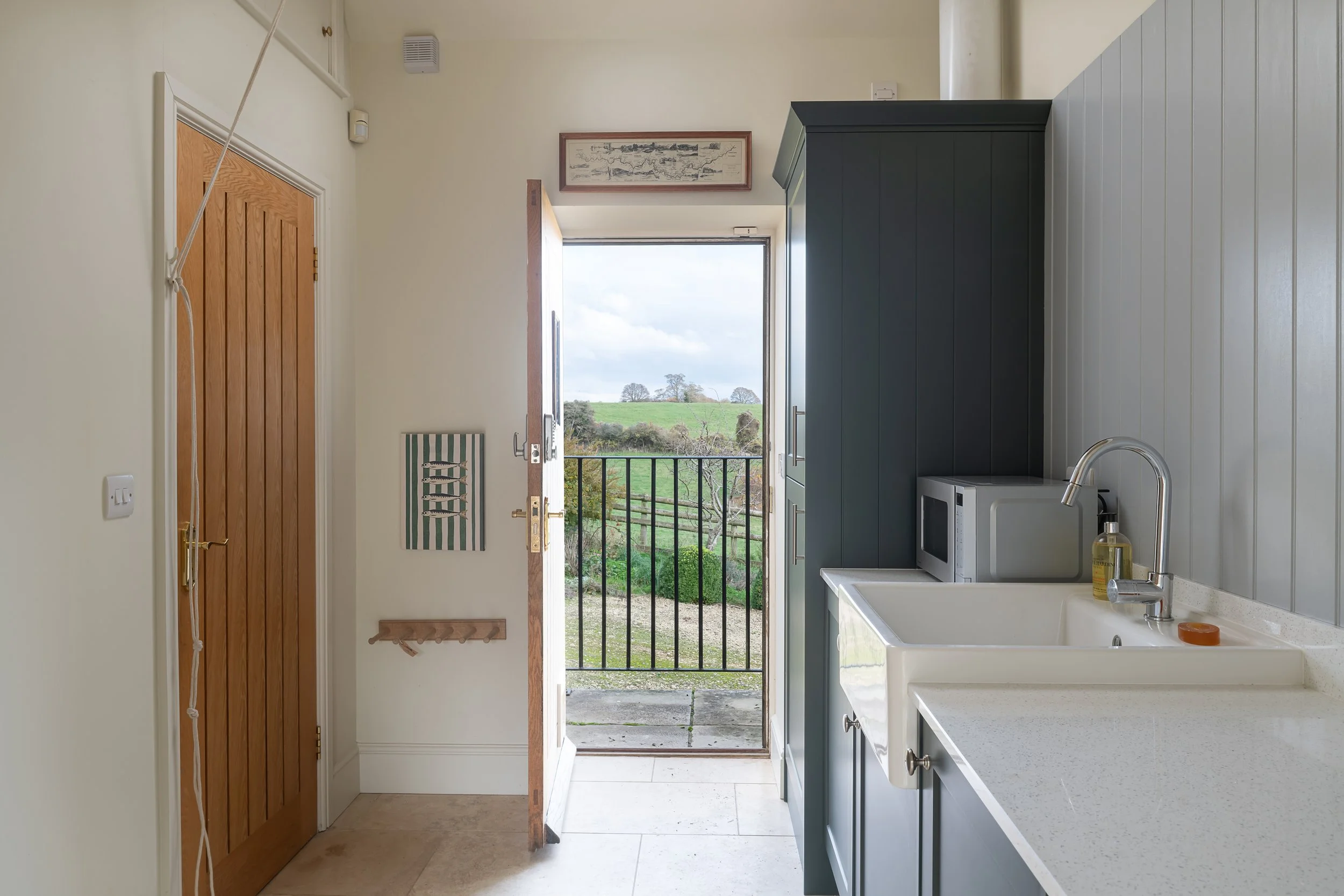 Kitchen with open door leading to a green outdoor landscape, blue cabinets, a microwave, sink, and various small items on the counter.