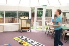 A woman playing shuffleboard in a sunlit indoor room with glass doors and a purple carpet.