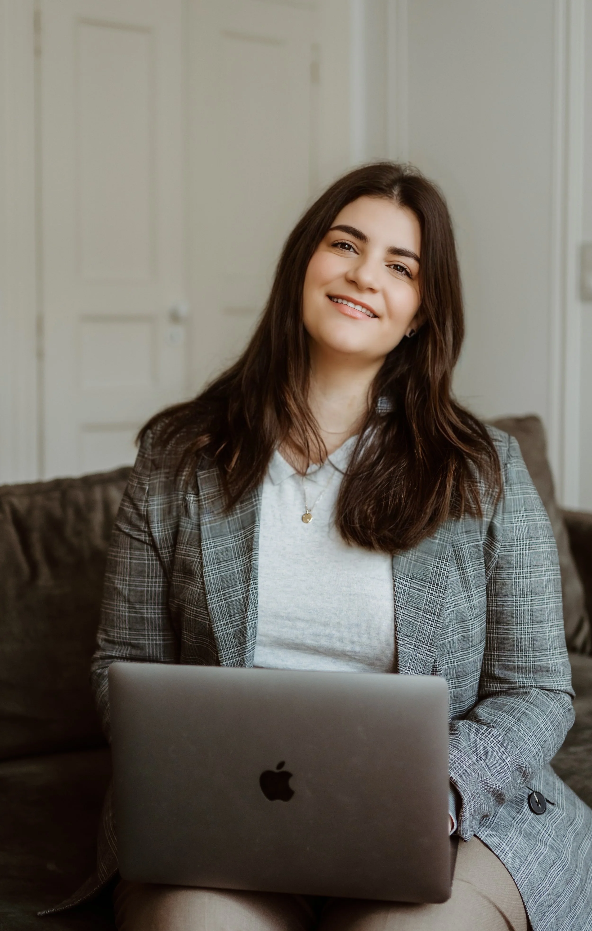Claudia, founder of Avalon, smiling and sitting on a couch with a laptop on her lap in an office setting.