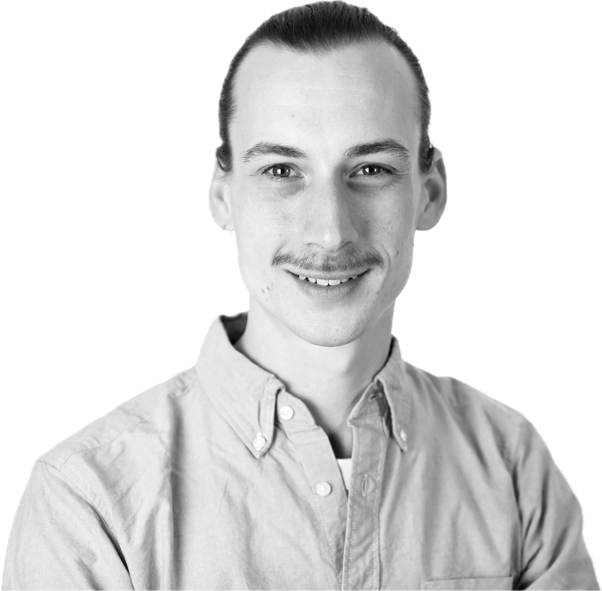 Schwarz-weiß-Bild eines lächelnden jungen Mannes mit Schulterlangem Haar, Schnäuzer, im Hemd, vor schwarz. Kombination aus freundlichem Gesicht und professioneller Kleidung.