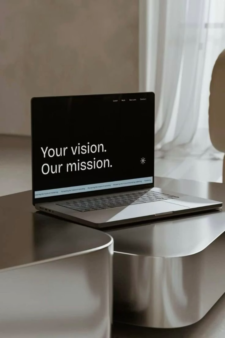 Un ordinateur portable ouvert sur une table avec l'écran affichant le texte "Your vision. Our mission." dans une pièce lumineuse aux rideaux blancs.