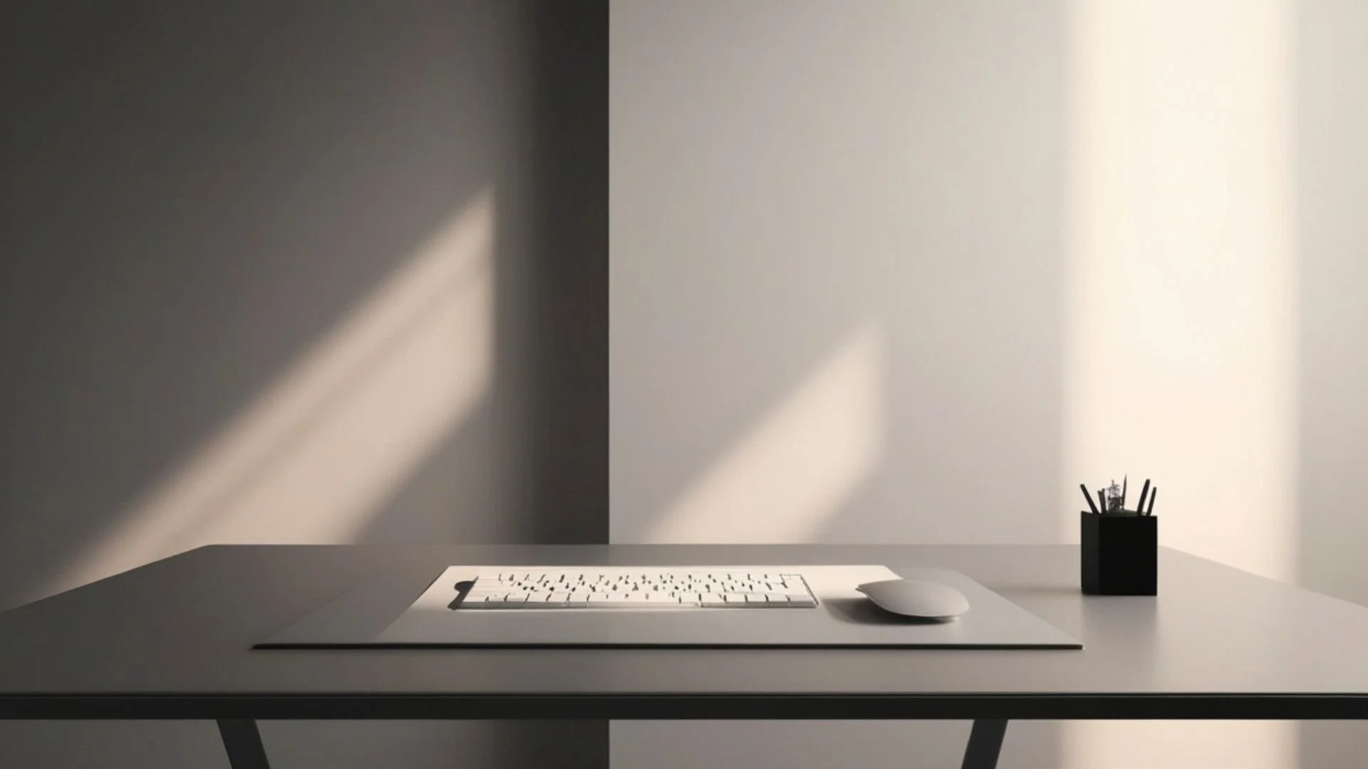 Un bureau minimaliste avec un clavier blanc, une souris blanche, et un porte-stylo noir avec des stylos, dans une pièce avec des murs contrastés, un côté sombre et un côté clair.