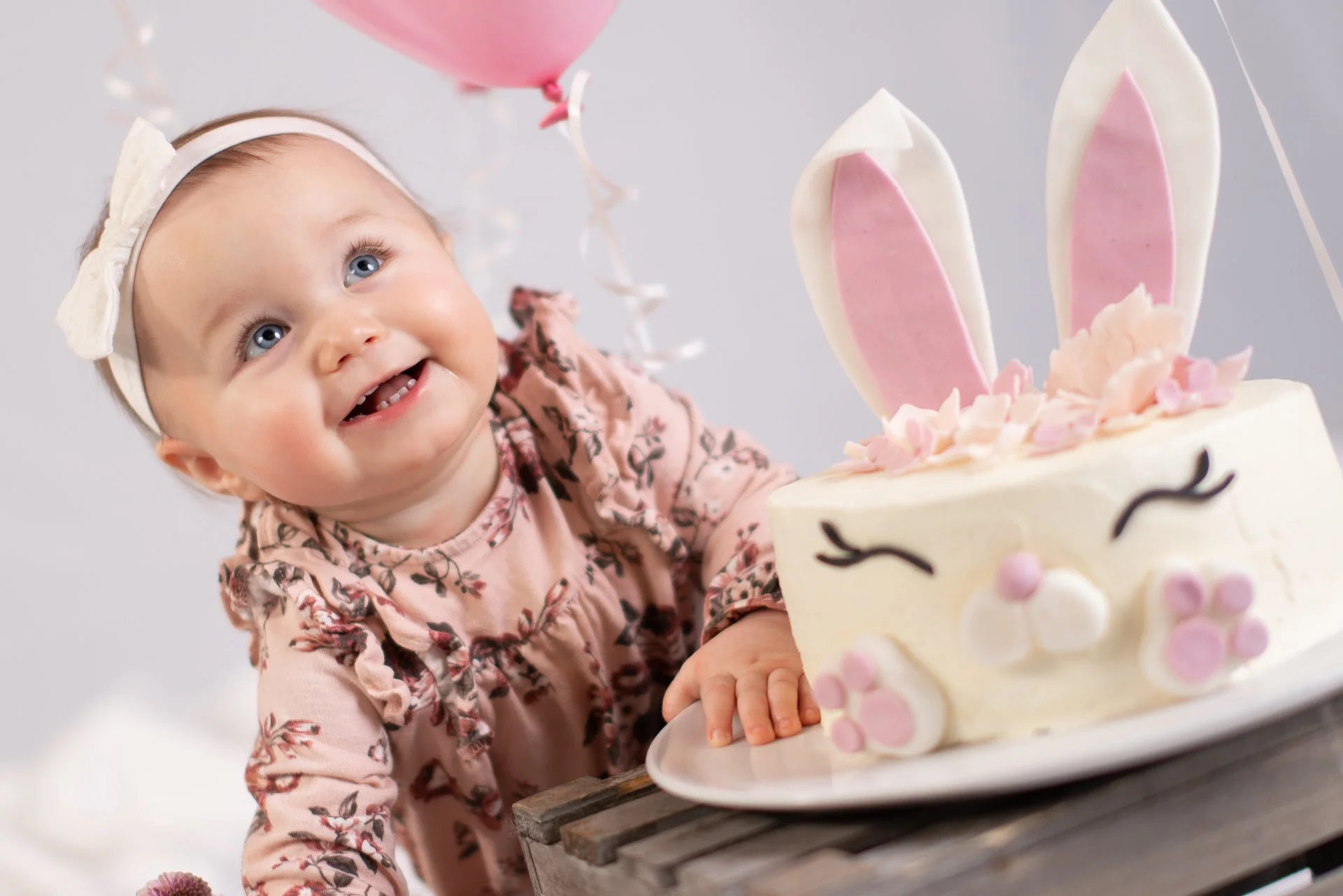 Aki Suomela valokuvaus portfolio. Syntymäpäiväsankarilla on iso kermainen kakku. Kakku on koristeltu vaaleanpunaisilla ja valkoisilla kukilla, ja kakun päällä on kaksi isoa pinkkiä ja valkoista kanin korvaa.