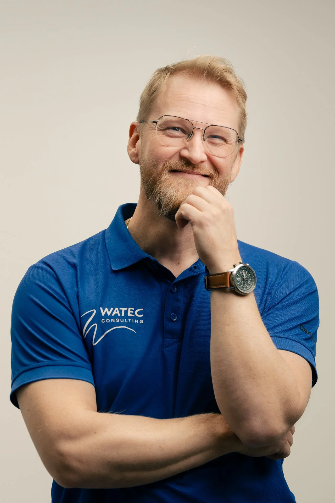 Aki Suomela valokuvaus portfolio. Henkilö hymyilee ja pitää kättä leuallaan, pukeutuneena siniseen pikeepaitaan