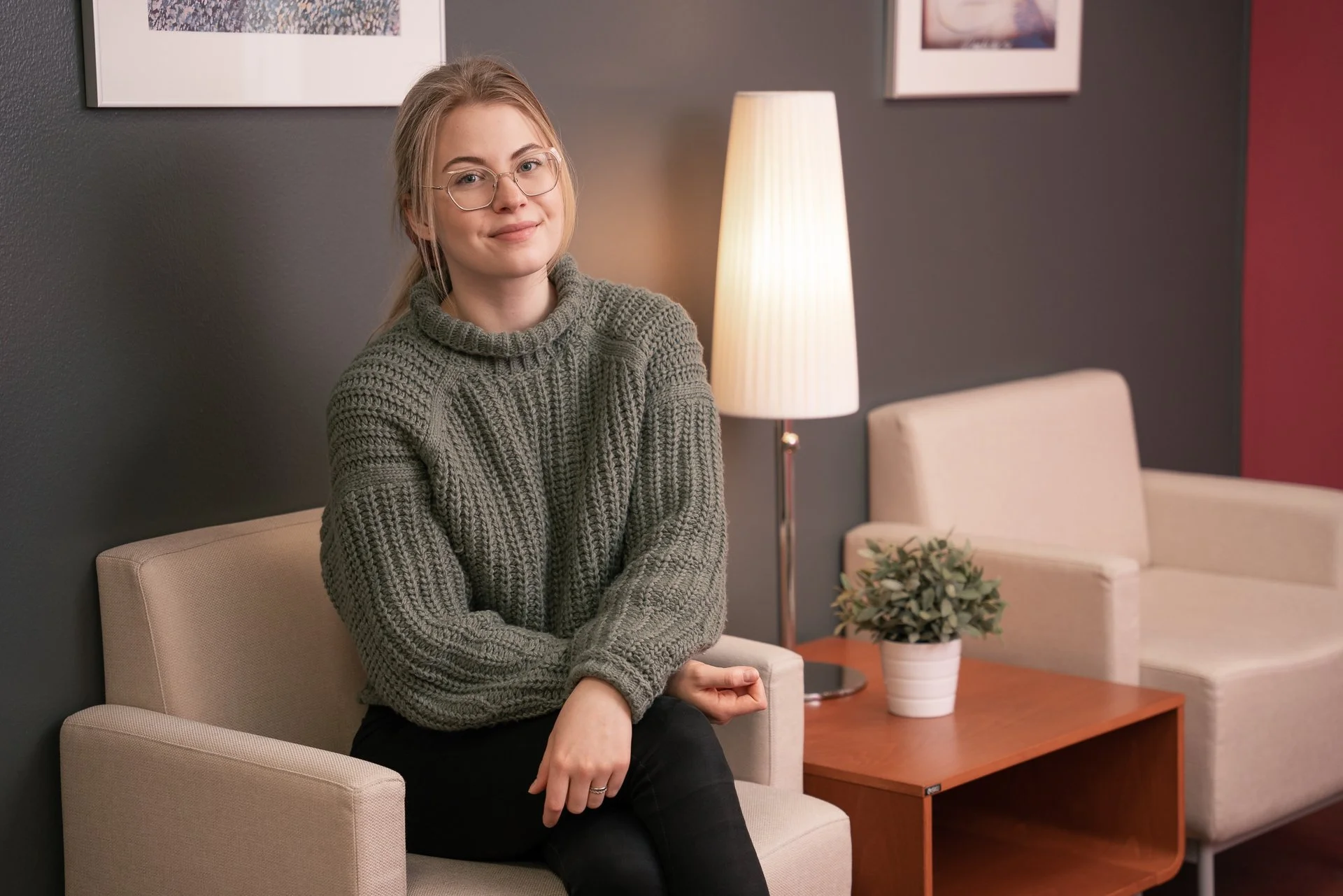 Aki Suomela valokuvaus portfolio. Nuori nainen istuu kerrossohvalla, huoneessa on lamppu ja kukka maljakossa pöydällä.